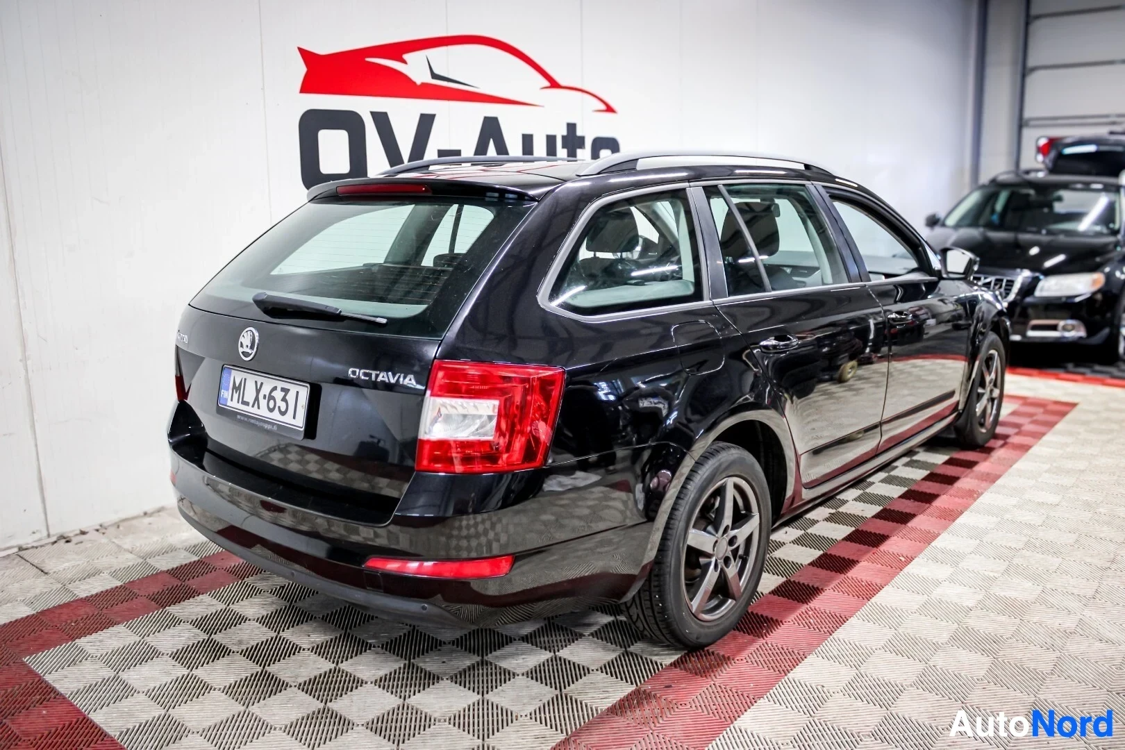 Takaviisto: Musta Skoda Octavia farmari auton oikea takakulma kuvattuna. Autossa on kattokiskot ja tummanharmaat kevytmetallivanteet. Rekisterikilpi näkyy takaluuku