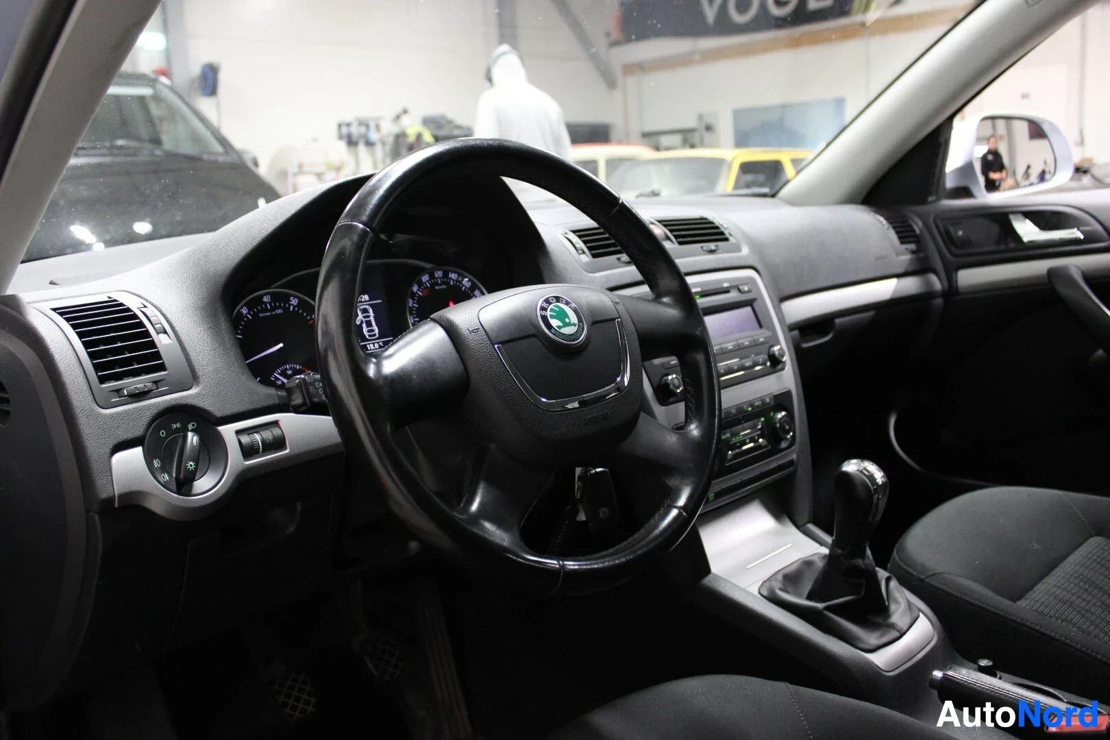 Ohjaamo: Kuva auton ohjaamosta kuljettajan puolelta. Kojelauta, mittaristo, ohjauspyörä Skoda-logolla ja vaihdekeppi ovat näkyvissä.