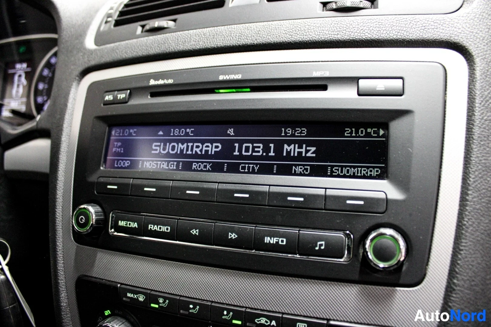 Yksityiskohta: Lähikuva auton keskikonsolin radiosta ja ilmastointipaneelista. Radion näytöllä lukee "SUOMIRAP 103.1 MHz".