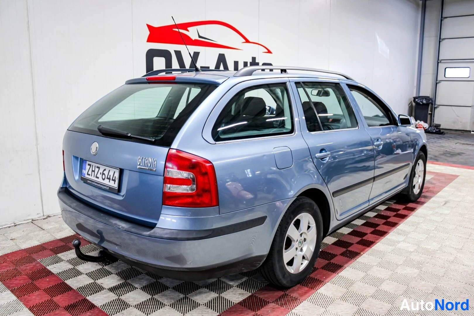 Takaviisto: Sininen Skoda Octavia Combi takaa viistosti kuvattuna sisätiloissa, rekisterikilpi, katukehäkatolla ja takavetojen puolella vetokoulu.