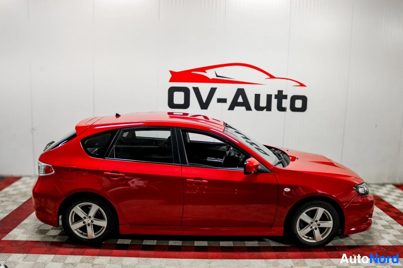 Sivulta: Punainen Subaru Impreza viistoperäinen auto sivusta katsottuna. Siinä on kevytmetallivanteet.
