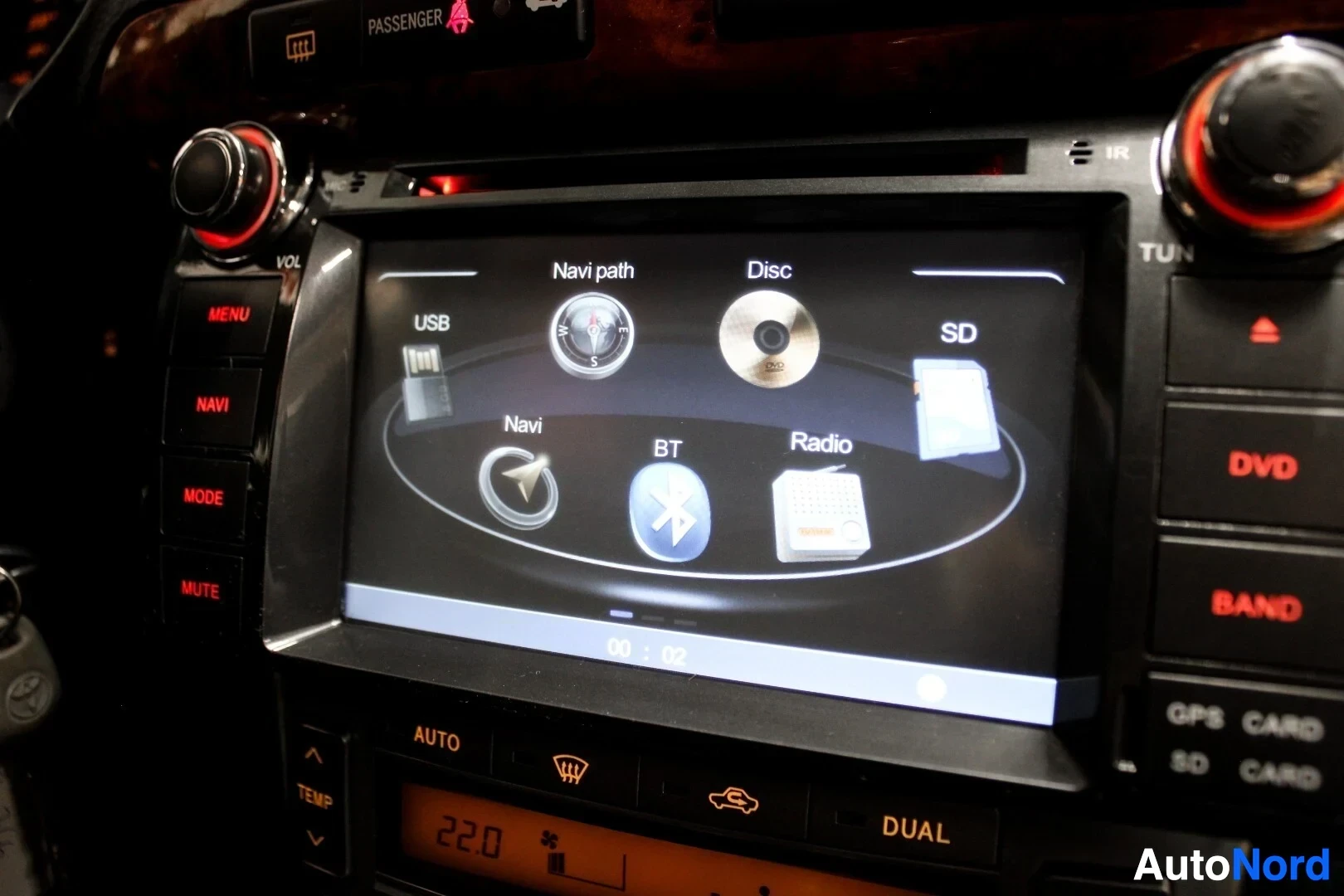 Yksityiskohta: Lähikuva auton infotainment-järjestelmän näytöstä, jossa näkyy päävalikko navigointi-, Bluetooth- ja radio-symboleilla.