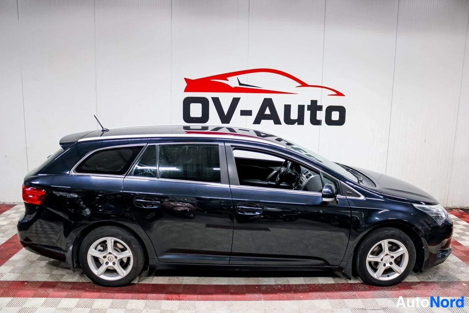 Sivulta: Tummanvärinen farmariauto oikealta sivulta kuvattuna parkkihallissa. Autossa on kevytmetallivanteet.