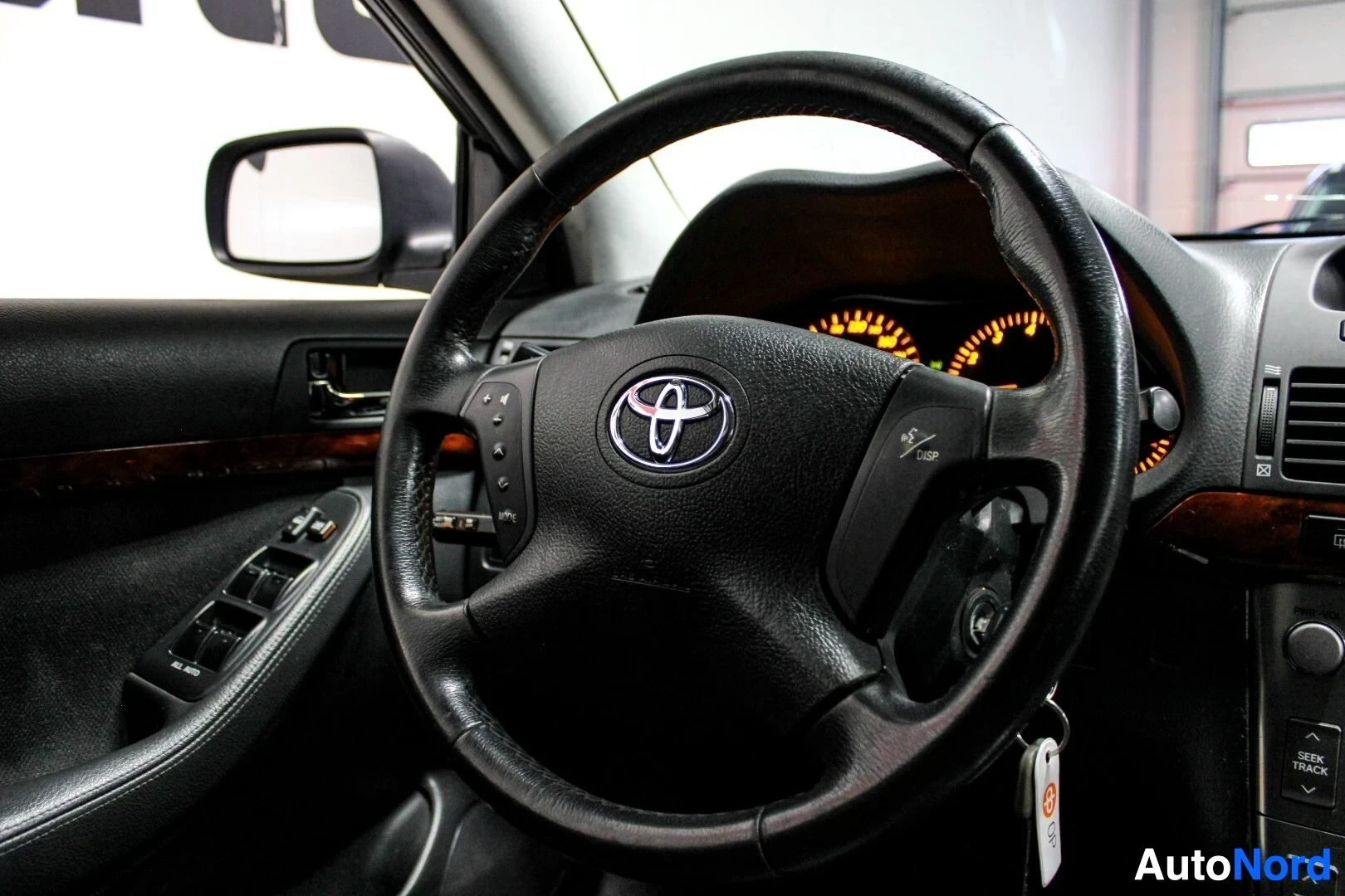 Yksityiskohta: Lähikuva auton ohjauspyörästä ja kuljettajan puolen oven hallintalaitteista. Ohjauspyörässä on Toyota-logo ja monitoimipainikkeet.