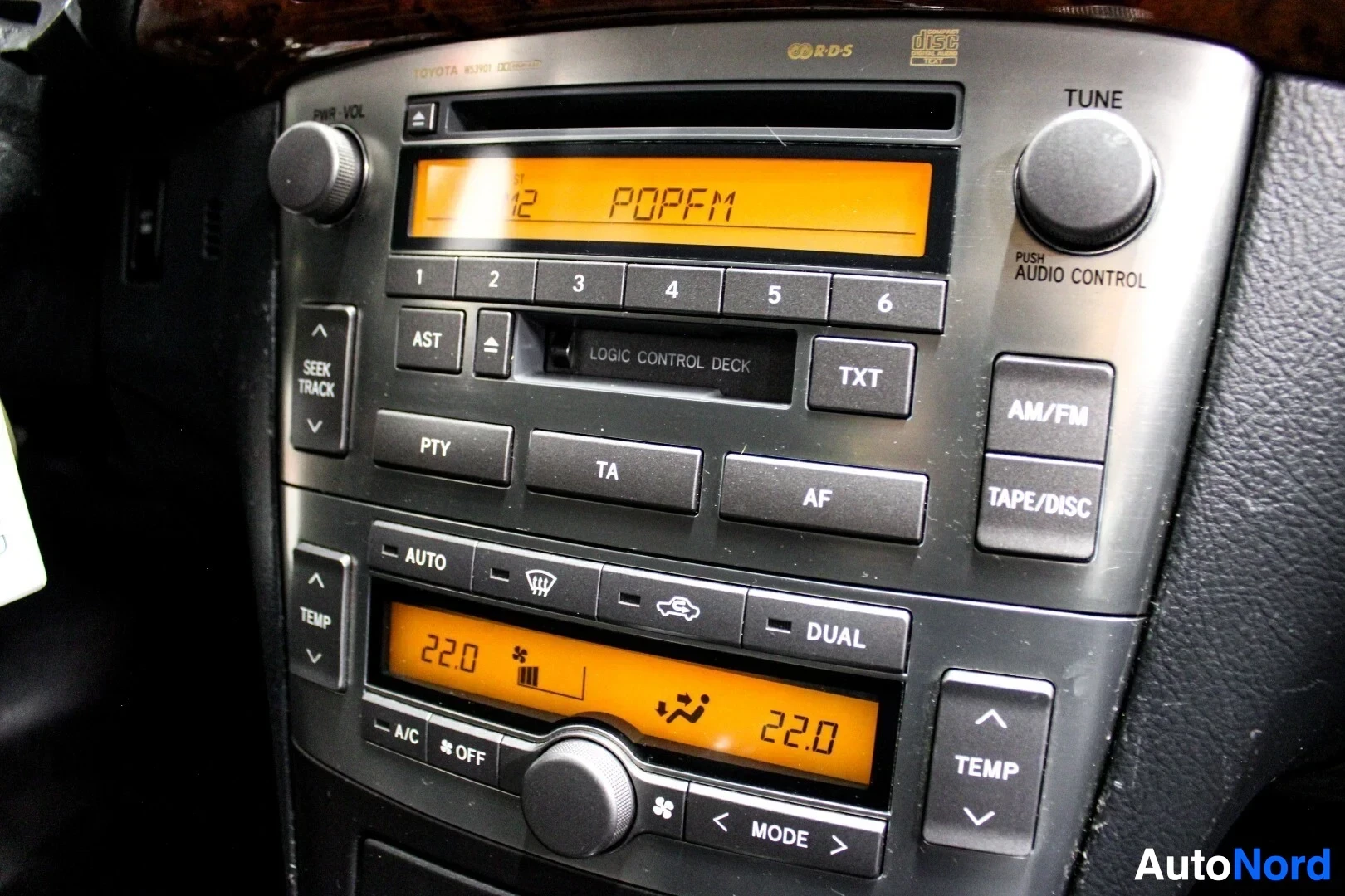 Yksityiskohta: Lähikuva auton keskikonsolin audio- ja ilmastointipaneeleista. Audionäytössä lukee 'POP FM' ja ilmastoinnissa '22.0'.