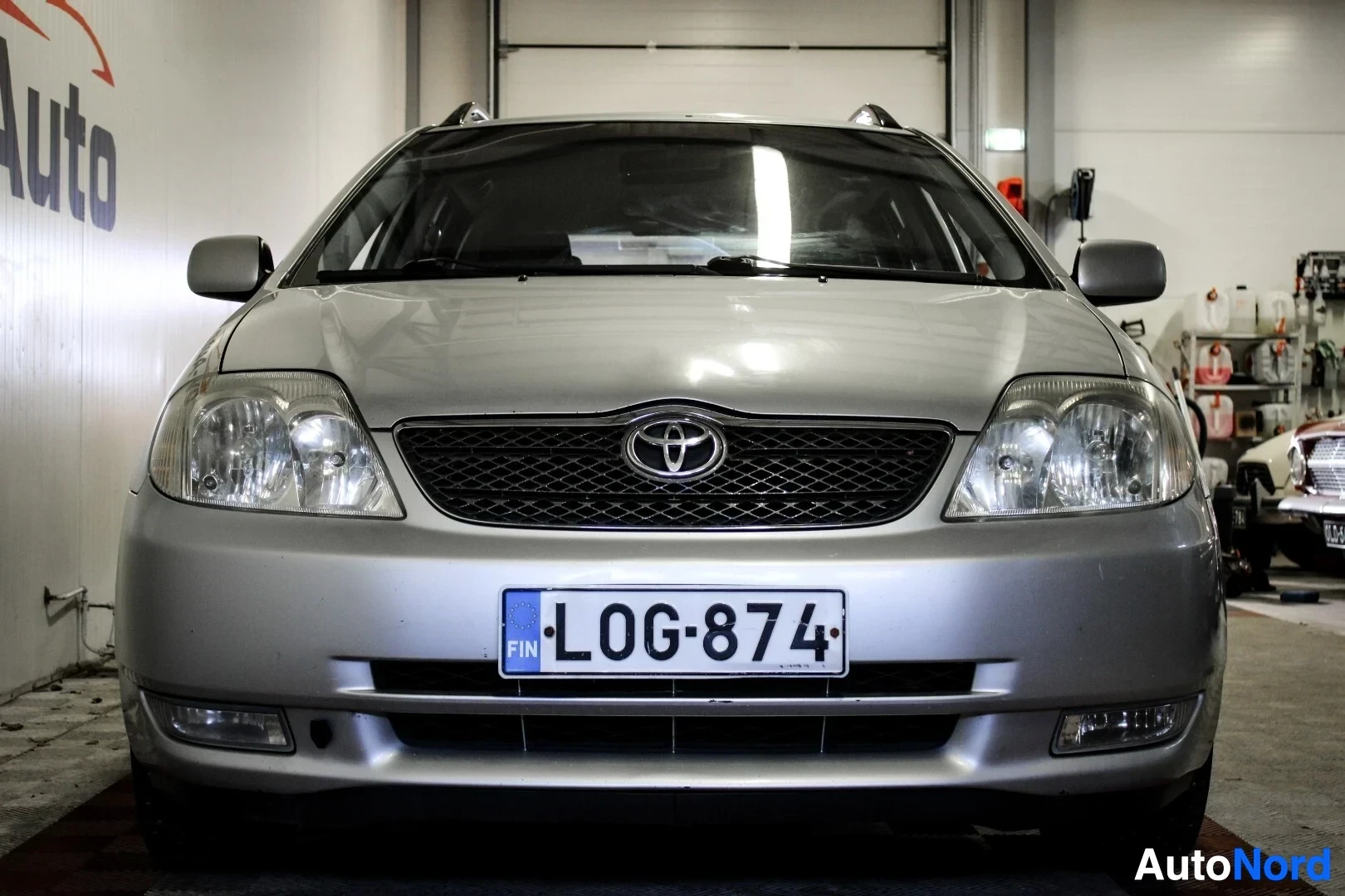 Edestä: Hopeanvärinen Toyota Corolla farmari edestä kuvattuna sisätilassa. Keulassa on Toyota-logo ja eturekisterikilpi.