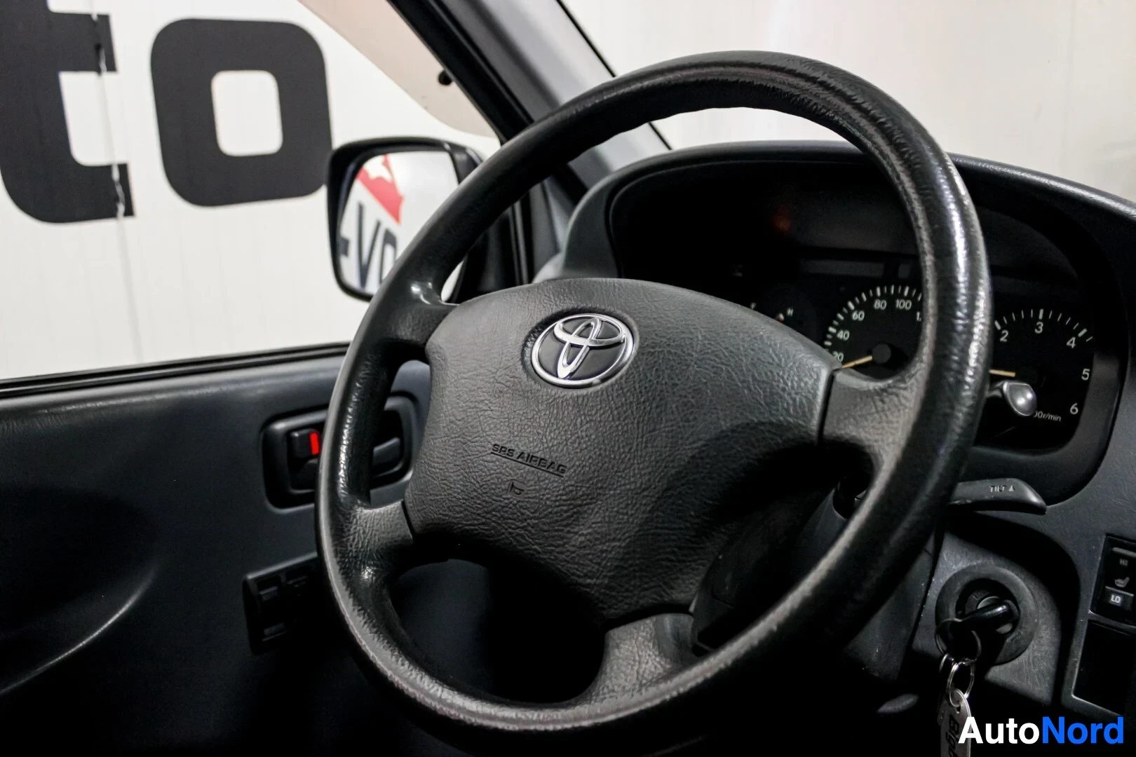 Ohjaamo: Kuljettajan ohjauspyörä, jossa näkyy Toyota-logo ja SRS AIRBAG -teksti. Ohjauspyörän takana näkyy mittaristo.