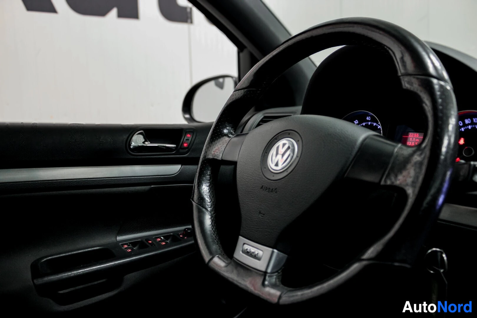 Yksityiskohta: Ohjauspyörän ja kuljettajan oven yksityiskohta. Ohjauspyörässä on VW-logo ja 'AIRBAG'-merkintä. Oviruudussa on sähköikkunoiden säätimet.
