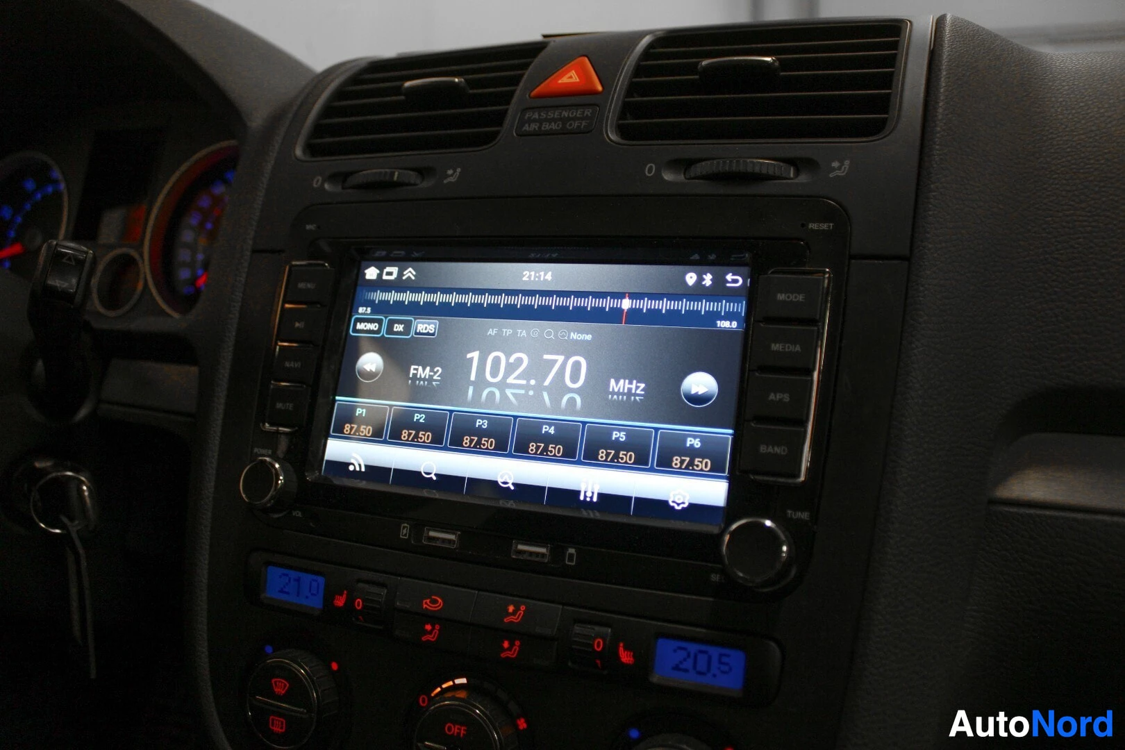 Ohjaamo: Lähikuva auton kojelaudasta, jossa näkyy kosketusnäyttö, joka näyttää FM-radion taajuuden 102.70 MHz ja useita esiasetettuja asemia.