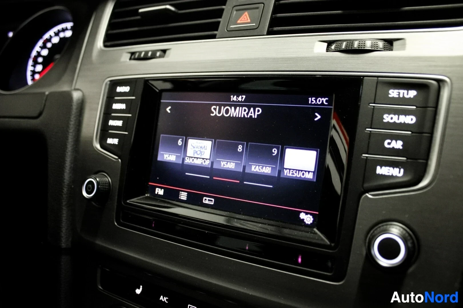 Yksityiskohta: Lähikuva auton infotainment-järjestelmän näytöstä, joka näyttää radiovalikon ja on asetettu kanavalle 'SUOMIRAP'. Näytöllä näkyy myös ulkolämpötila 15.0°C ja ke