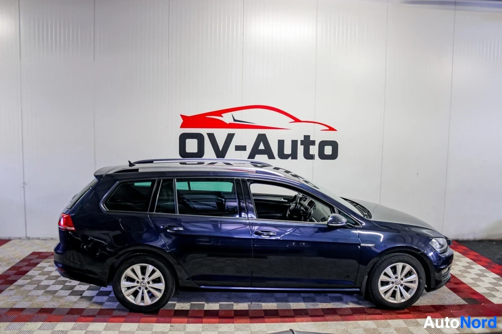 Sivulta: Tumman farmariauton vasen kylki autohallissa. Autossa on kattokaiteet ja kevytmetallivanteet.