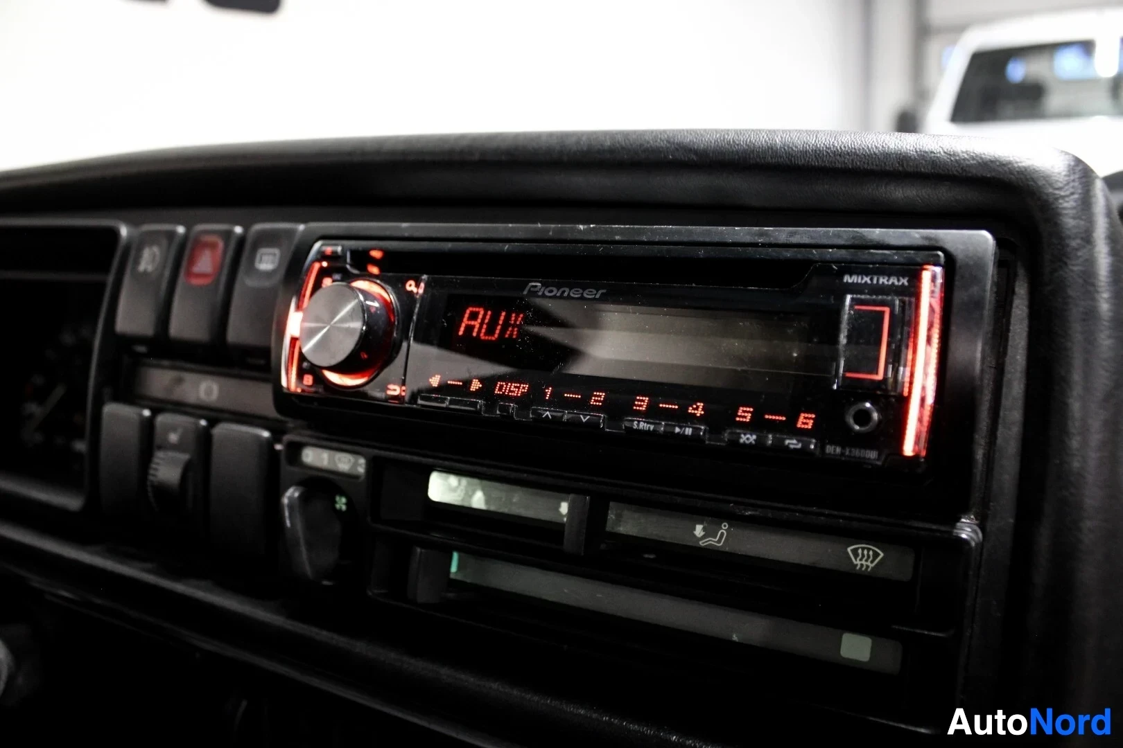 Yksityiskohta: Lähikuva kojelaudasta, jossa on Pioneer-merkkinen autostereo punaisella näytöllä ja painikkeiden valaistuksella. Stereoiden alapuolella on autoon integroitu ilm