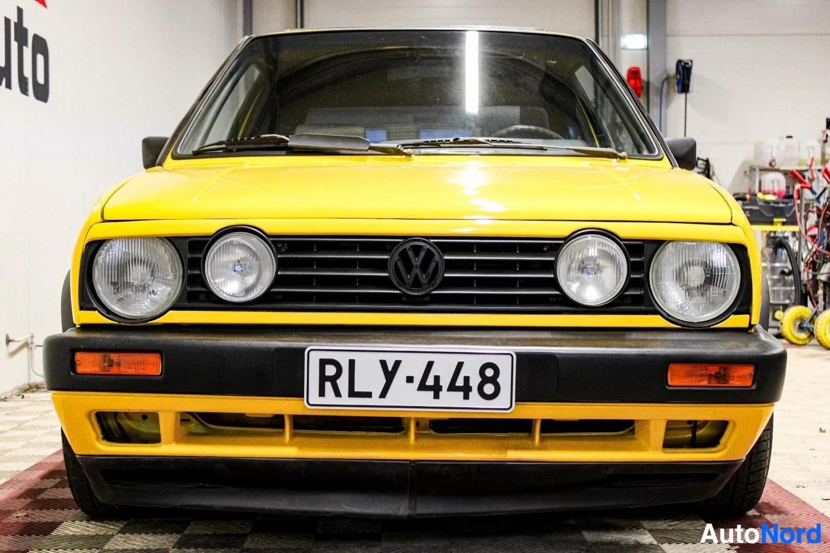 Edestä: Keltaisen auton etuosa edestäpäin kuvattuna sisätiloissa. Autossa on pyöreät ajovalot ja musta etupuskuri.