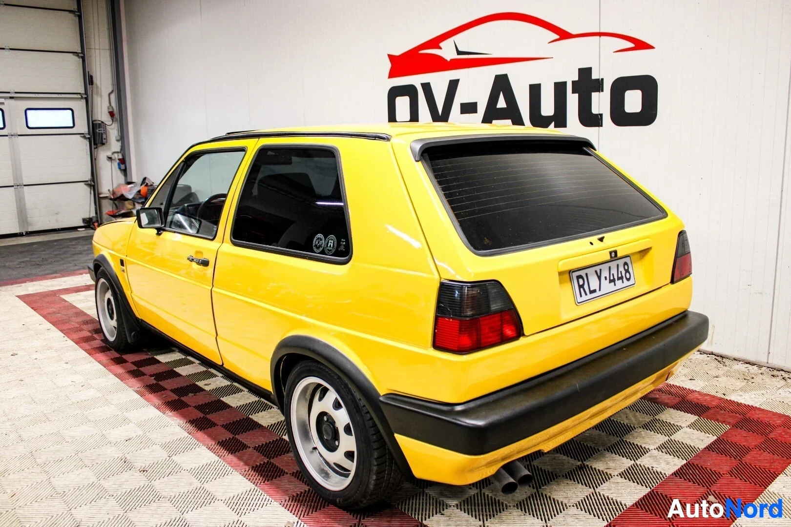 Takaviisto: Keltainen kaksiovinen hatchback, jossa on mustat puskurit ja takaspoileri, kuvattuna takaviistosta. Autossa on rekisterikilpi "" ja kaksi pakoputken ulos