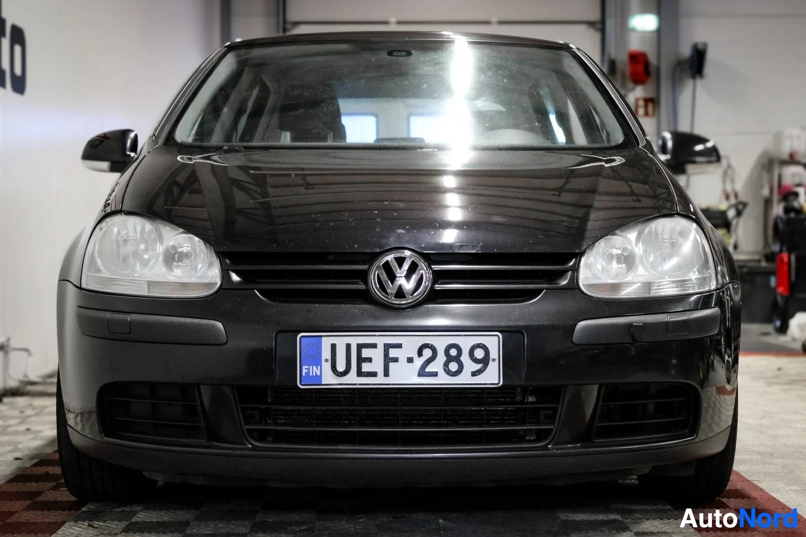 Edestä: Musta Volkswagen Golf edestä päin kuvattuna. Keulassa on Volkswagen-logo ja rekisterikilpi. Valo heijastuu tuulilasista