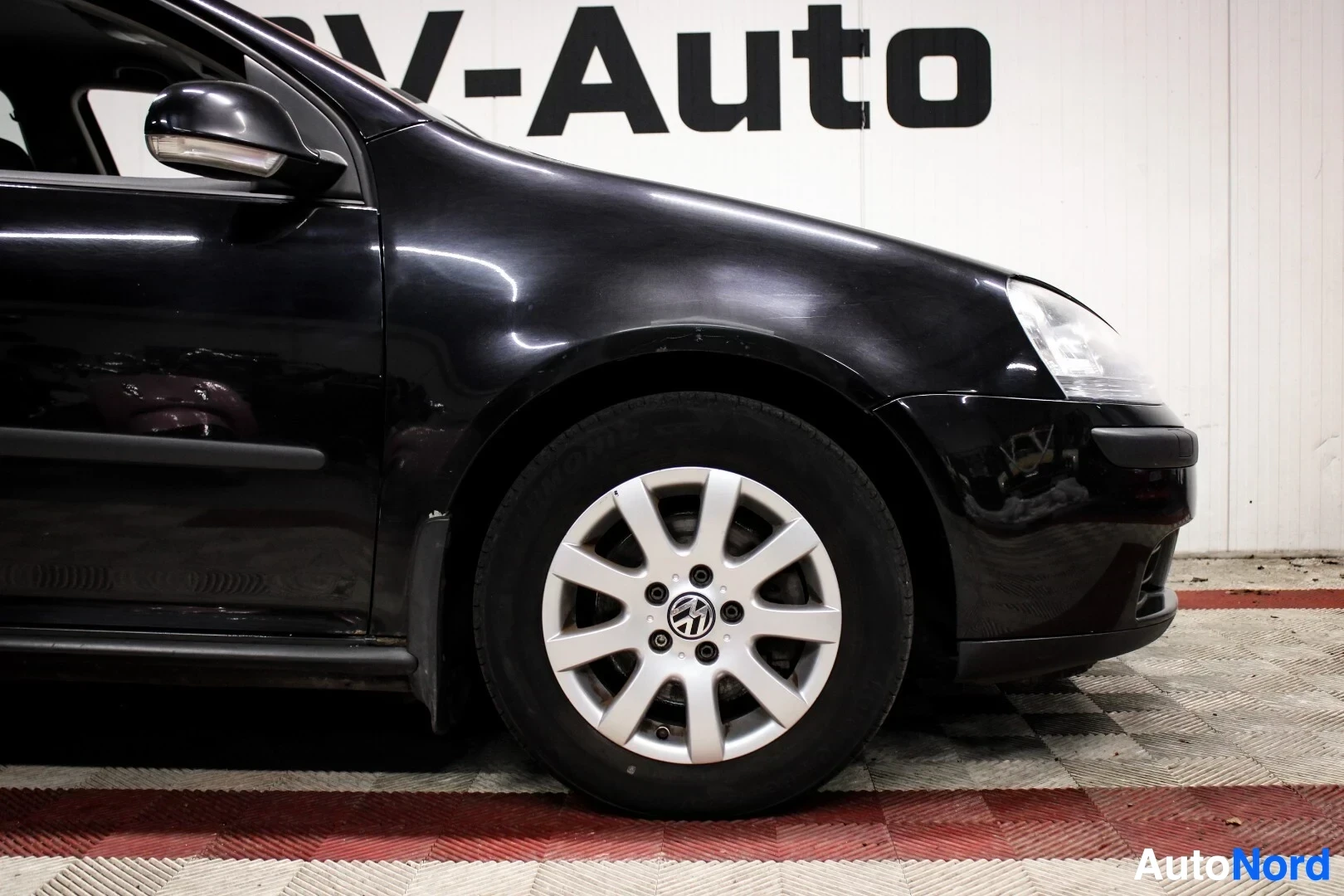 Yksityiskohta: Lähikuva henkilöauton oikean etupyörän alueesta. Vanteessa näkyy kahdeksan puolaa ja keskellä Volkswagenin logo.
