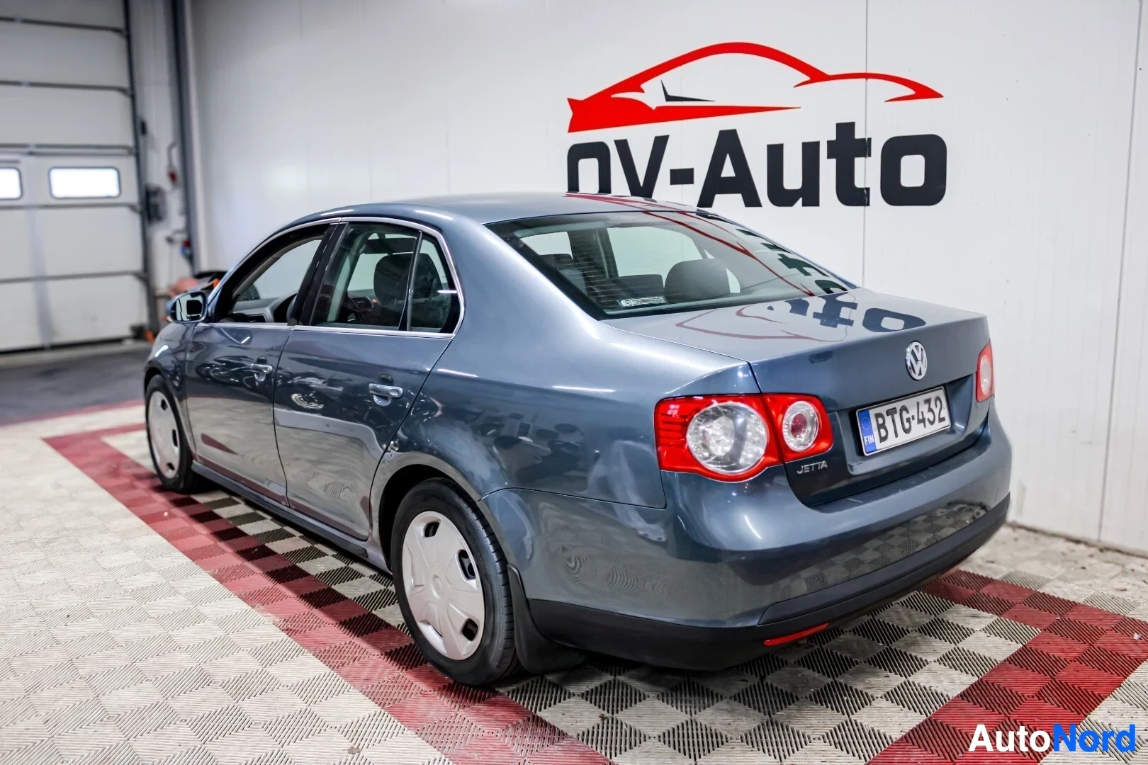 Takaviisto: Harmaa henkilöauto kuvattu takaa oikealta puolelta, taka- ja kylkikolmanneskuva. Autossa on umpiovanteet.
