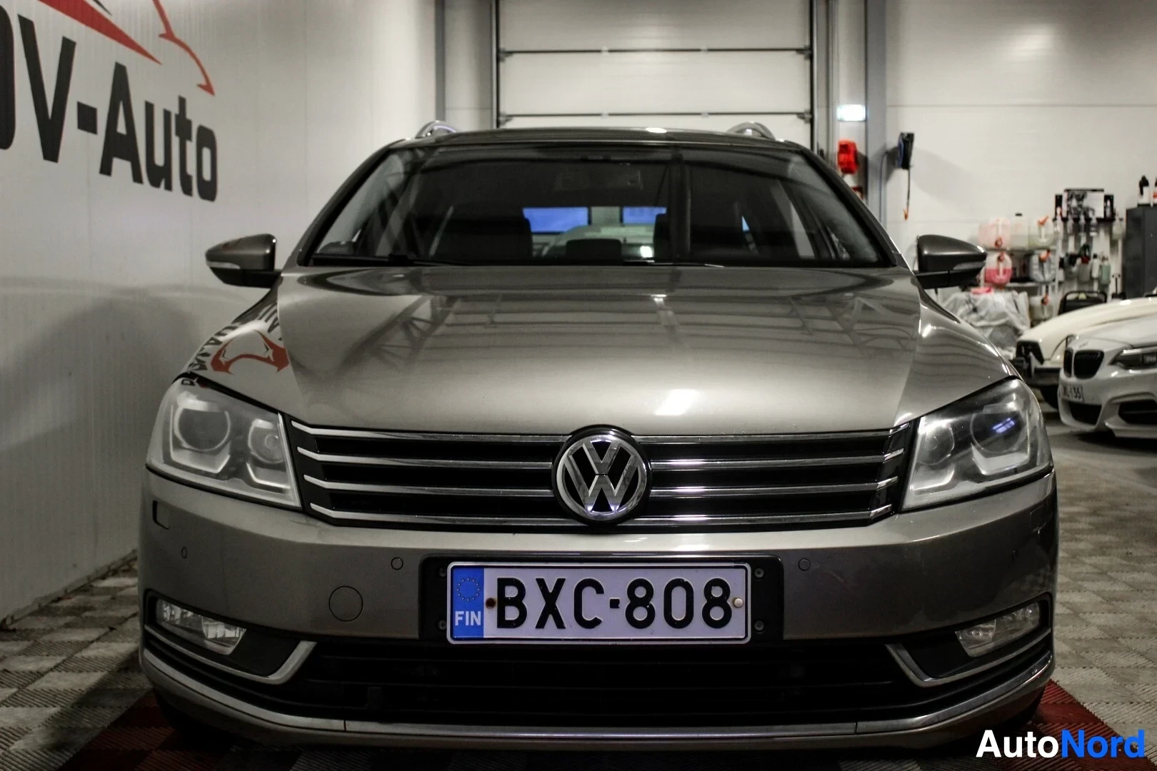 Edestä: Harmaan farmariauton etuosa, jossa on Volkswagen-logo ja rekisterikilpi. Autossa on päiväajovalot