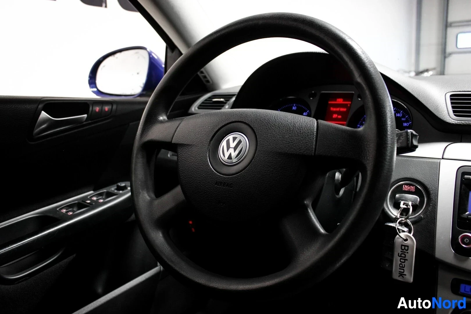 Ohjaamo: Lähikuva auton ohjauspyörästä, jossa on Volkswagen-logo keskellä, ja osasta kuljettajan ovea, jossa näkyy ikkunoiden ohjauspainikkeet.