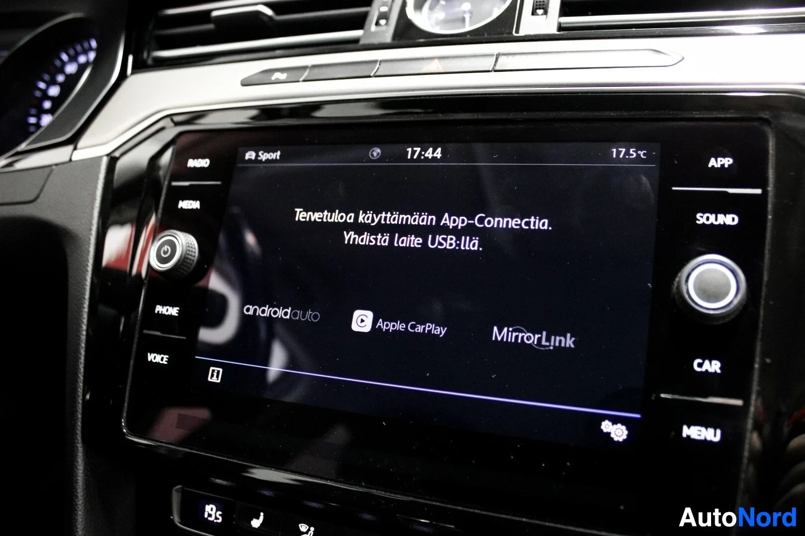 Ohjaamo: Tarkka kuva auton infotainment-järjestelmän näytöstä, jossa lukee "Tervetuloa käyttämään App-Connectia. Yhdistä laite USB:llä.". Näytöllä on myös Android Auto-