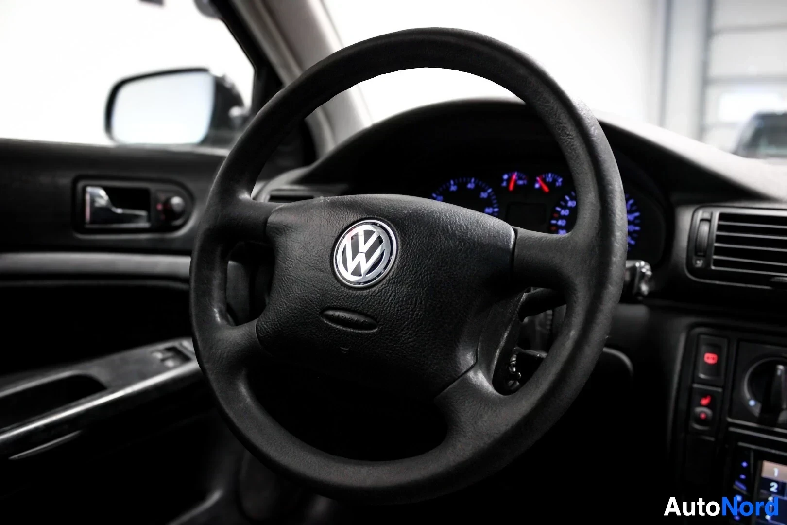Ohjaamo: Lähikuva ohjauspyörästä, jossa on Volkswagen-logo keskellä. Taustalla näkyy auton mittaristo.