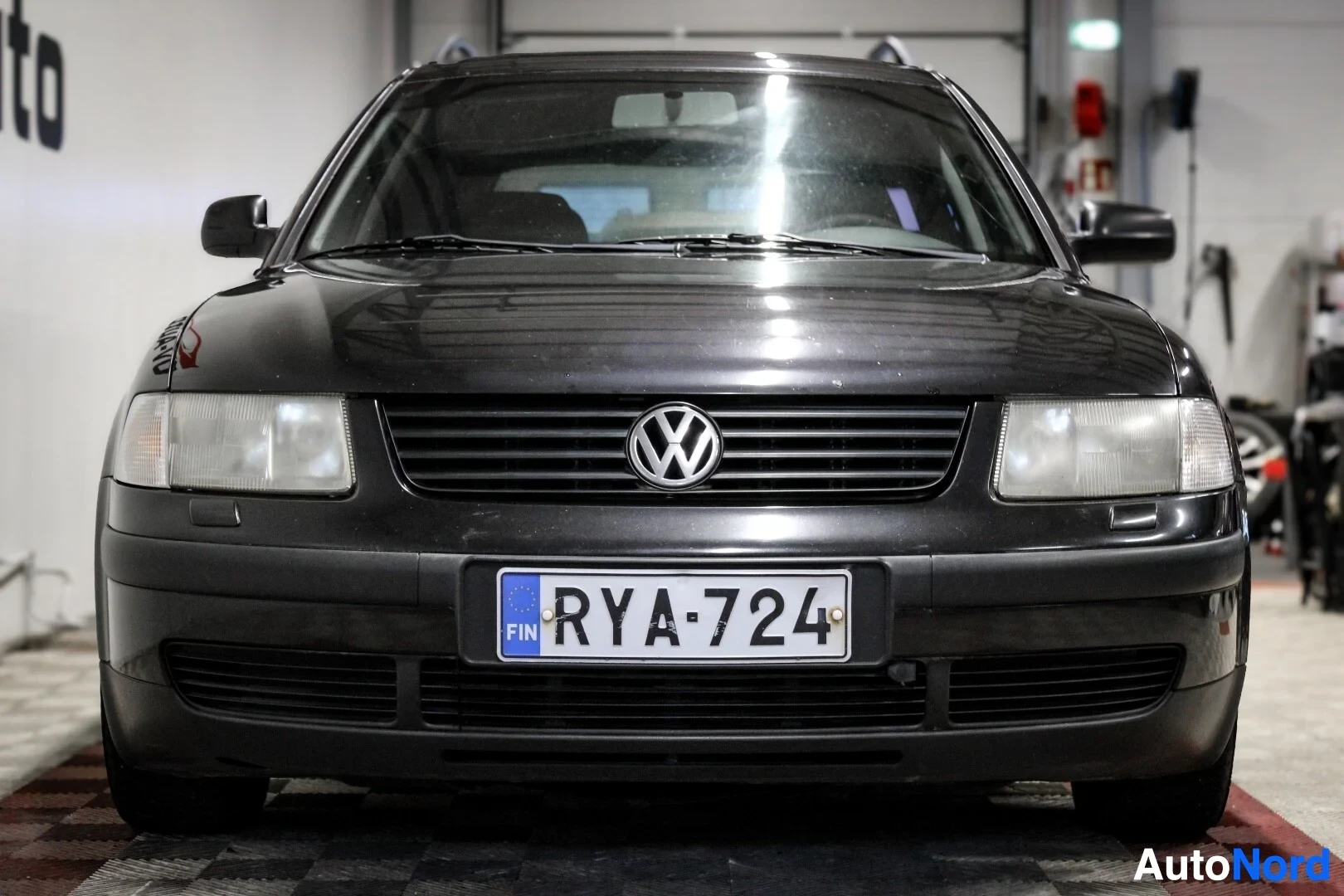 Edestä: Auton etuosa edestäpäin kuvattuna. Rekisterikilpi "" on näkyvissä. Etuvalot ovat kellertävät ja naarmuuntuneet. Ajoneuvon logon "VW" näkyy edessä