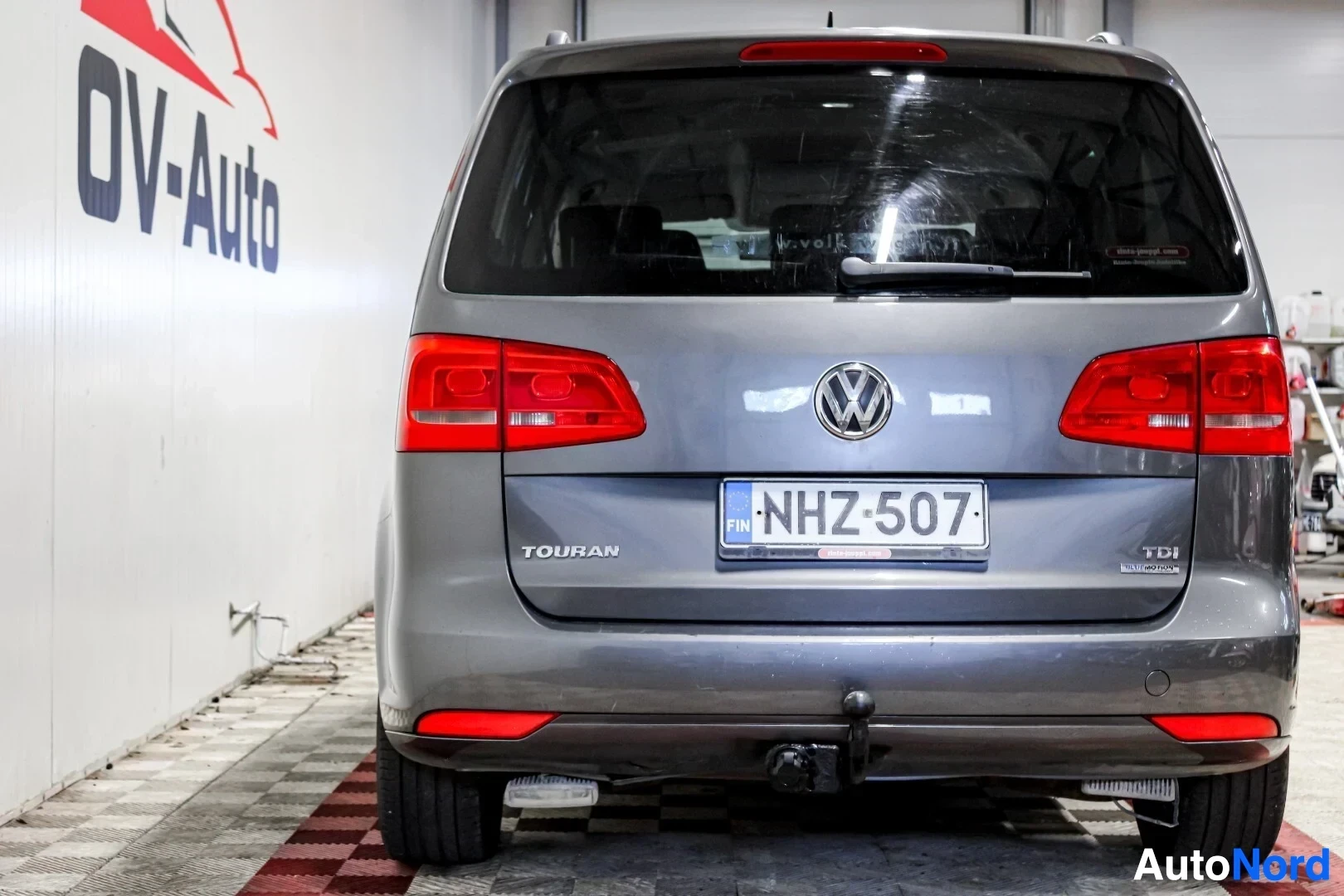 Takaa: Harmaa henkilöauto kuvattuna takaa suoraan. Rekisterikilpi on asennettu. Vetokoukku näkyy takapuskurin alla