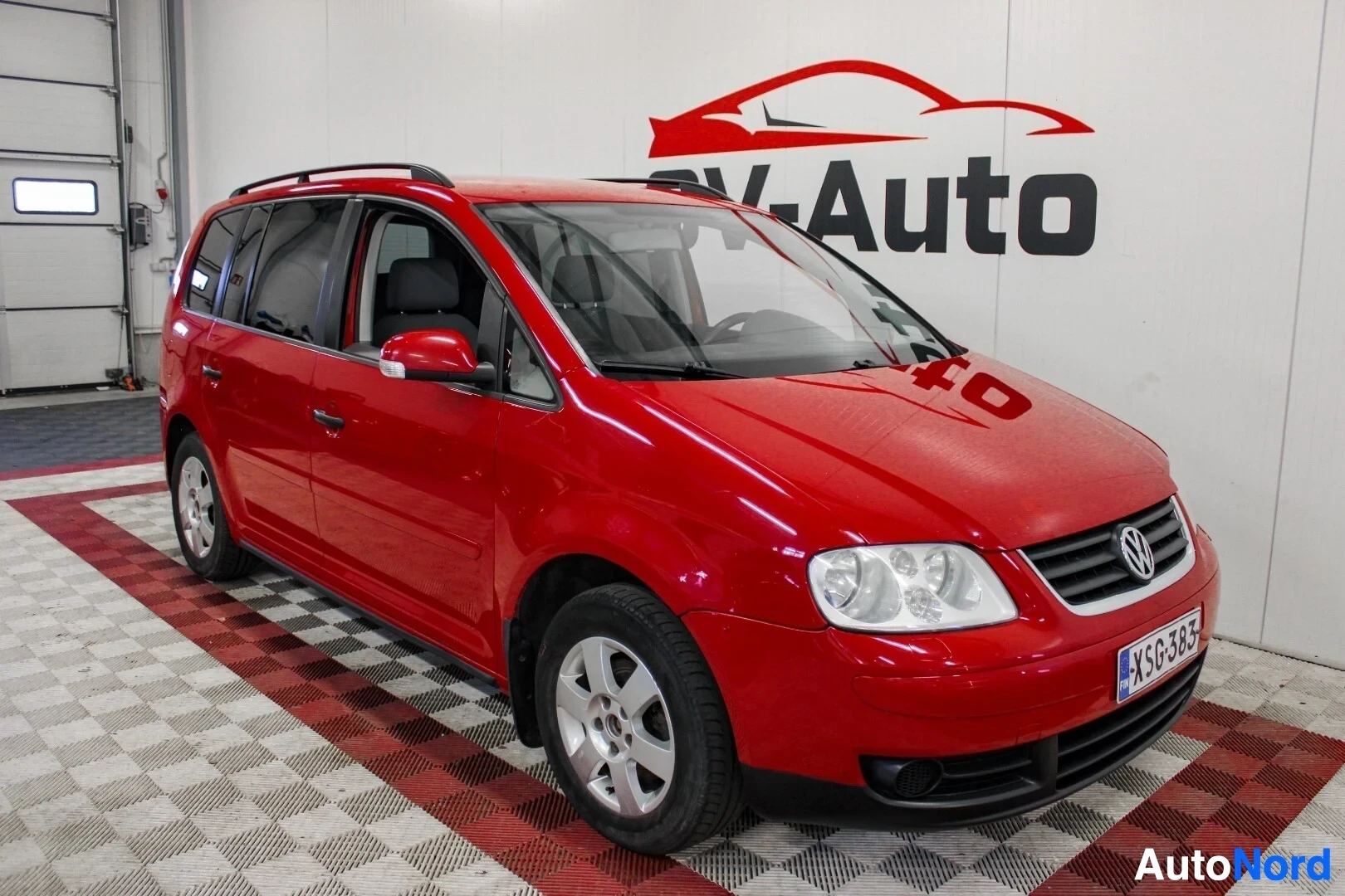 Etuviisto, nokka oikealle: Punainen Volkswagen-henkilöauto kuvattuna edestä ja oikealta sivulta viistosti. Autossa on kattokiskot ja kevytmetallivanteet.