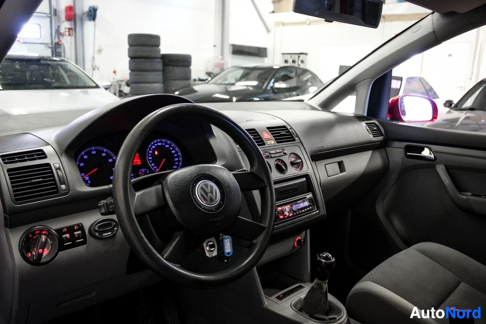 Ohjaamo: Kuvassa näkyy auton kojelauta, mittaristo ja ohjauspyörä, jossa on Volkswagen-logo. Keskikonsolissa on radionäyttö ja ilmastoinnin säätimet. Auton sisusta on ha