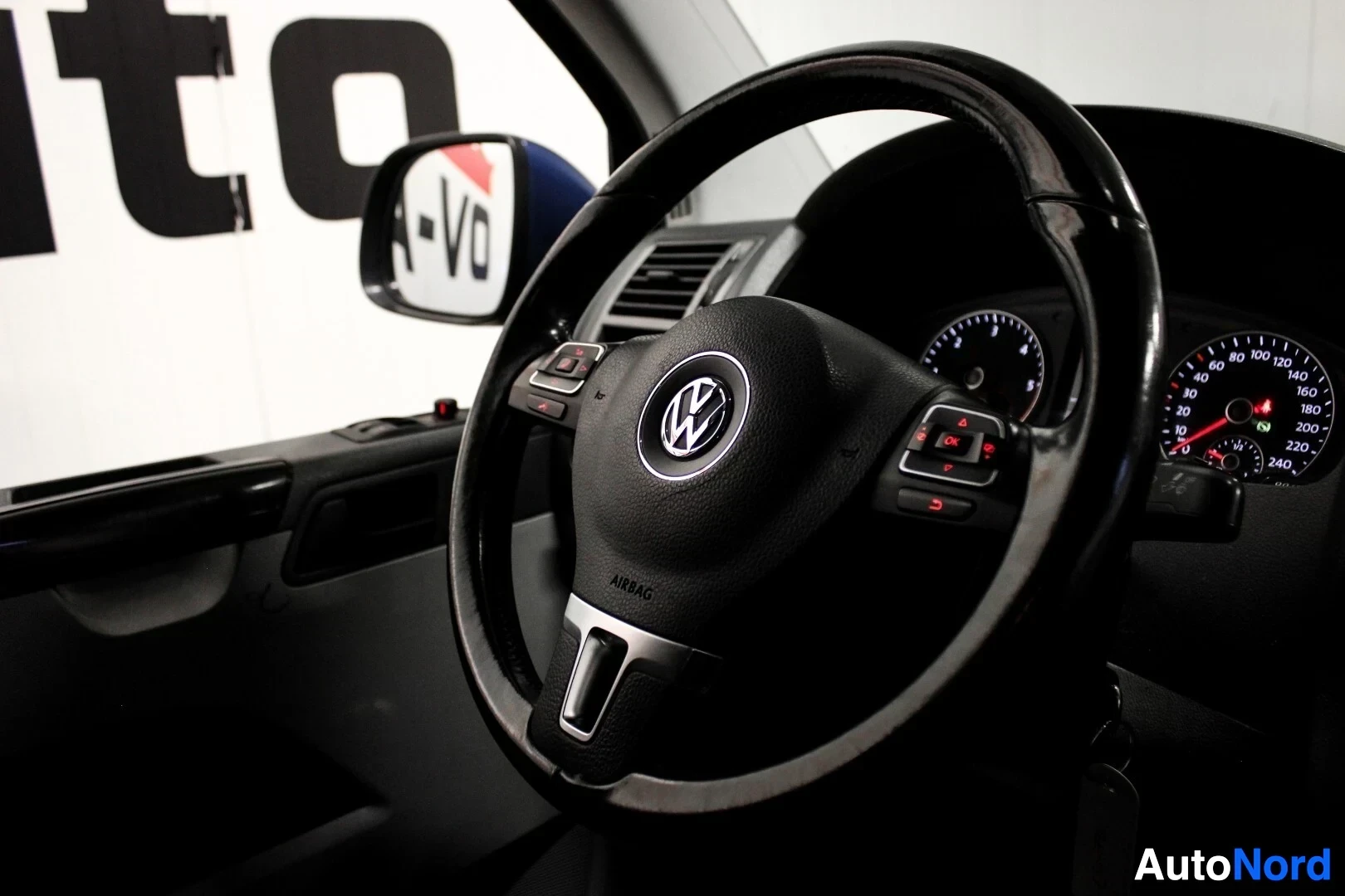 Yksityiskohta: Lähikuva ohjauspyörästä, jossa on hopeanvärinen Volkswagen-logo ja painikkeita. Mittaristo on osittain näkyvissä taustalla.