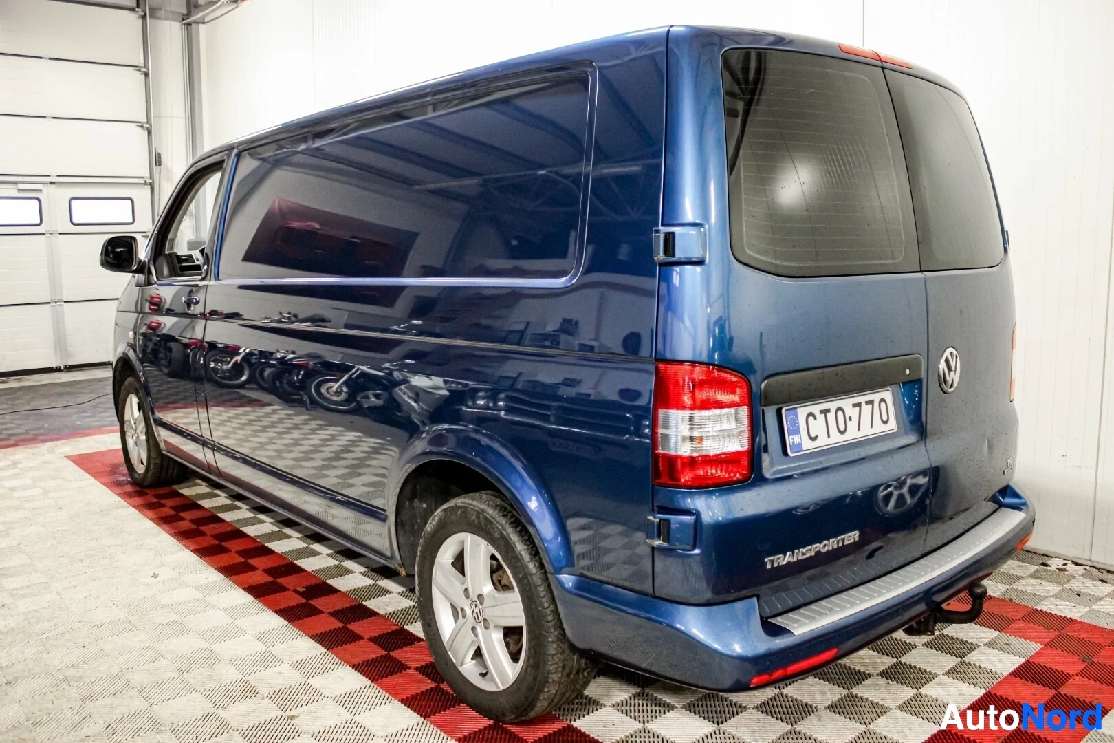 Takaviisto: Sininen pakettiauto myyntihallissa. Kuvassa näkyy ajoneuvon takaosa ja oikea kylki.