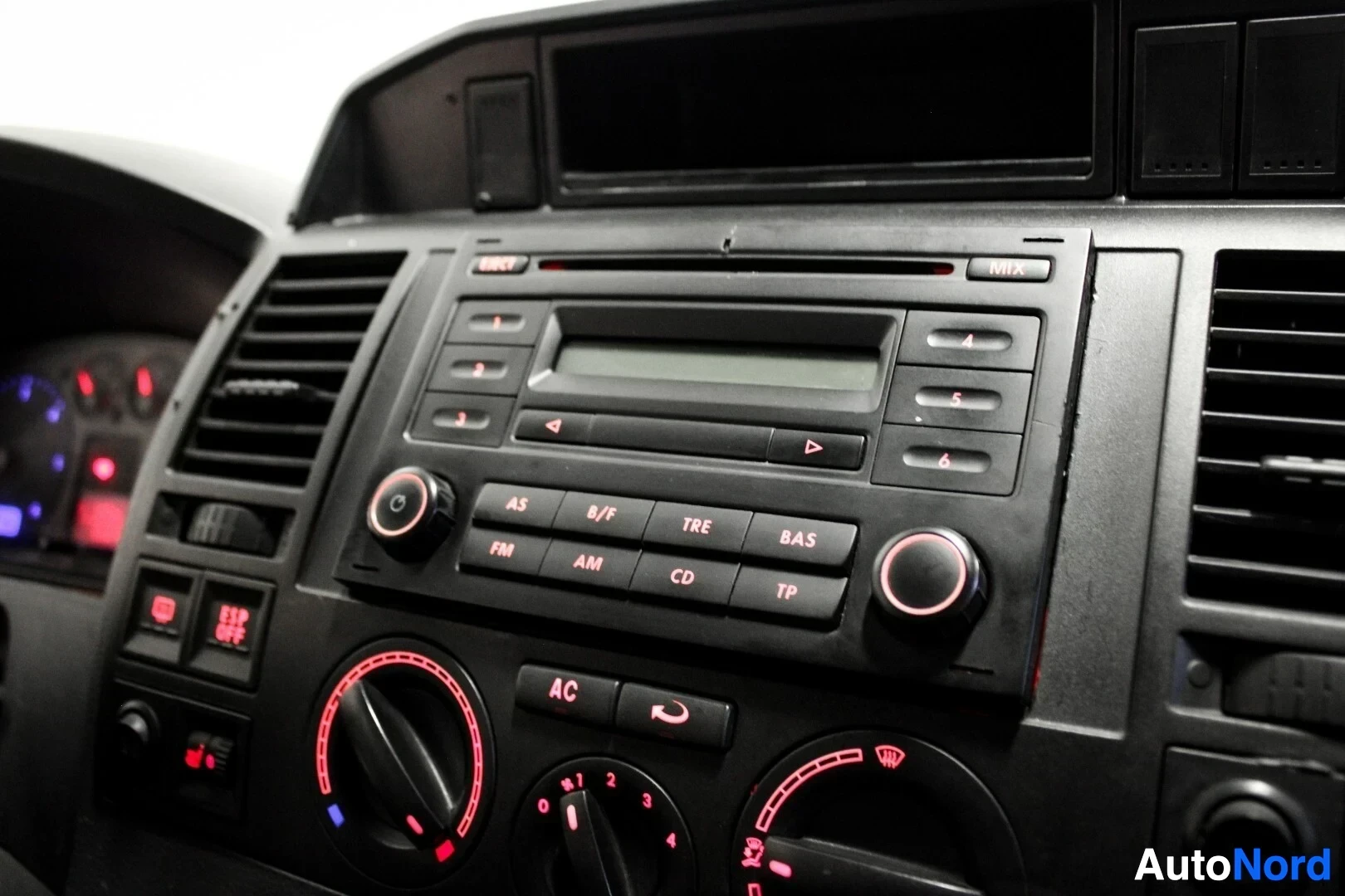 Yksityiskohta: Lähikuva ajoneuvon keskikonsolista. Siinä on radio CD-soittimella ja useilla painikkeilla (esim. FM, AM, CD, TP). Alapuolella on pyöreät ilmastointisäätimet ja