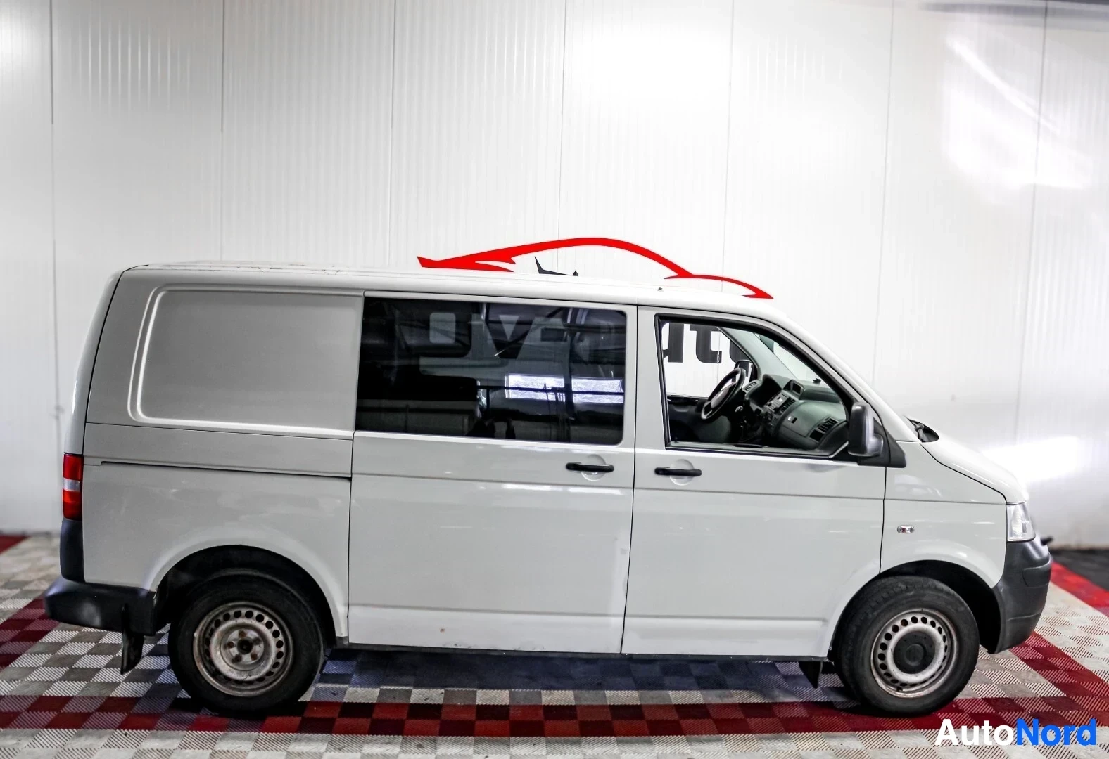 Sivulta: Valkoinen pakettiauto on kuvattu vasemmalta sivulta sisätiloissa. Autossa on umpinainen tavaratila takana ja lasit etuovissa.