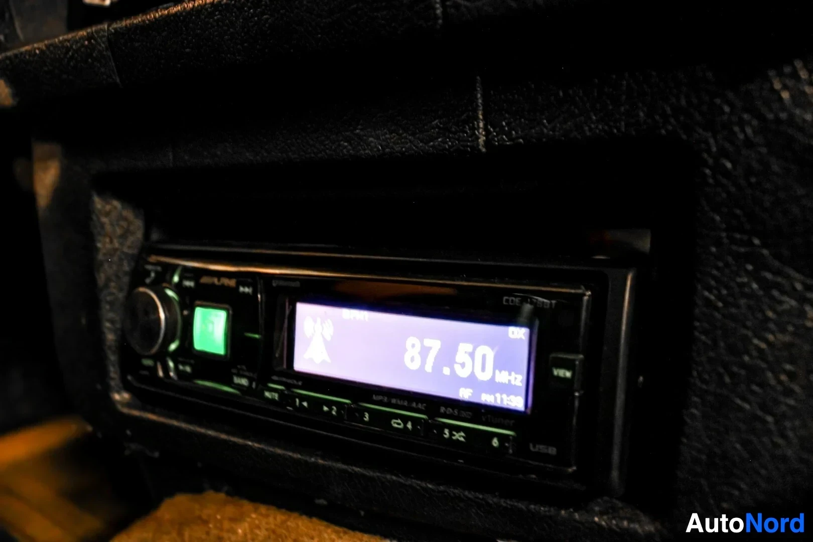 Yksityiskohta: Lähikuva autostereosta, jossa on näyttö ja painikkeita. Näytössä lukee "87.50 MHz" ja "USB".