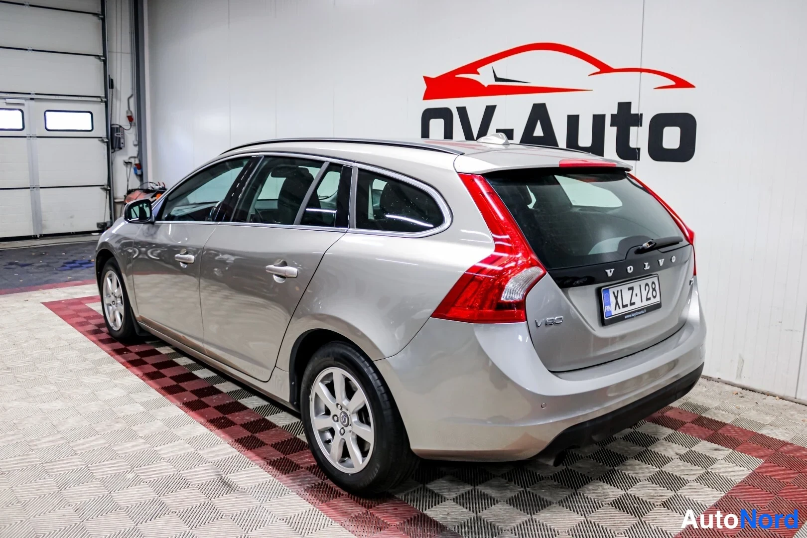 Takaviisto: Hopeanharmaa farmariauto takaa sivulta valoisassa autotallissa; rekisterikilpi ja VOLVO-merkintä takaluukussa näkyvät.