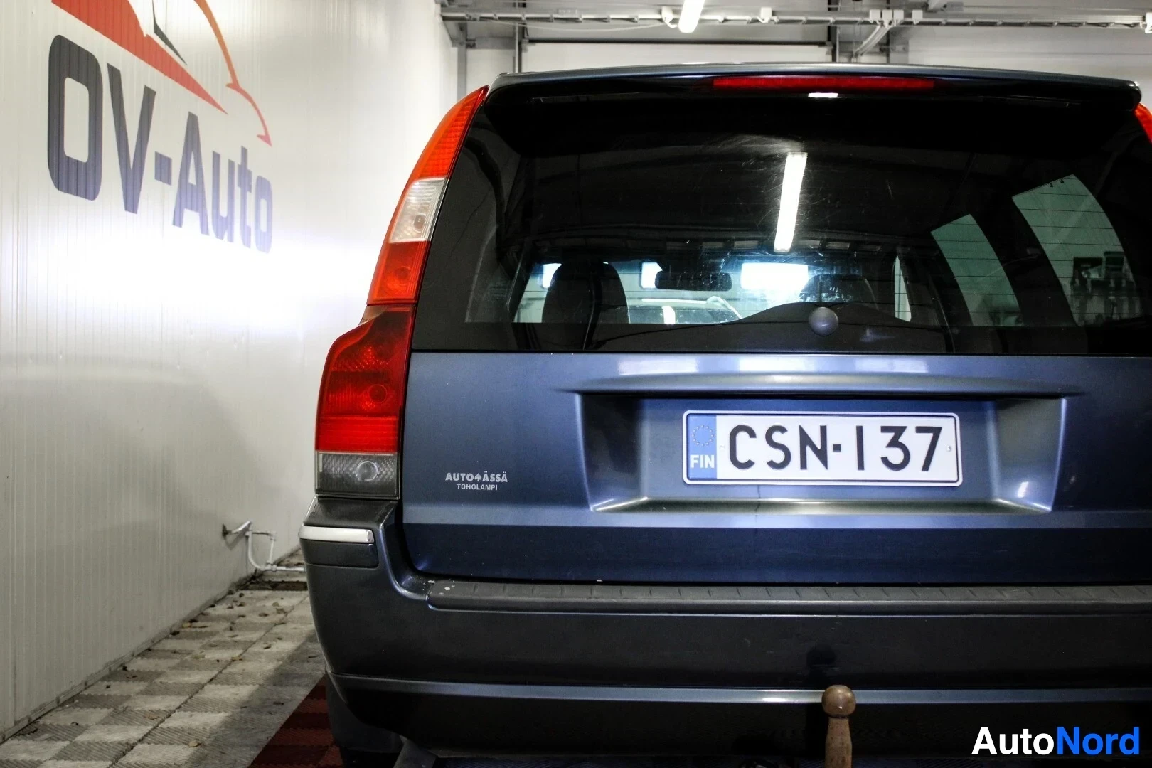 Takaa: Tummanharmaa farmariauto takaa kuvattuna. Rekisterikilpi on selkeästi näkyvillä. Takaluukussa on tarra, jossa lukee 'AUTO+ASSA TUOHILAMPI'