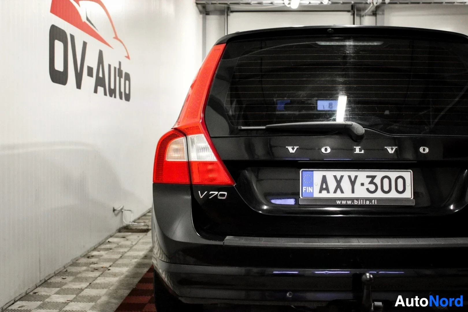 Takaa: Musta farmariauto kuvattuna suoraan takaa. Auton rekisterikilvessä lukee ja peräkontin luukussa 'VOLVO' ja 'V70'