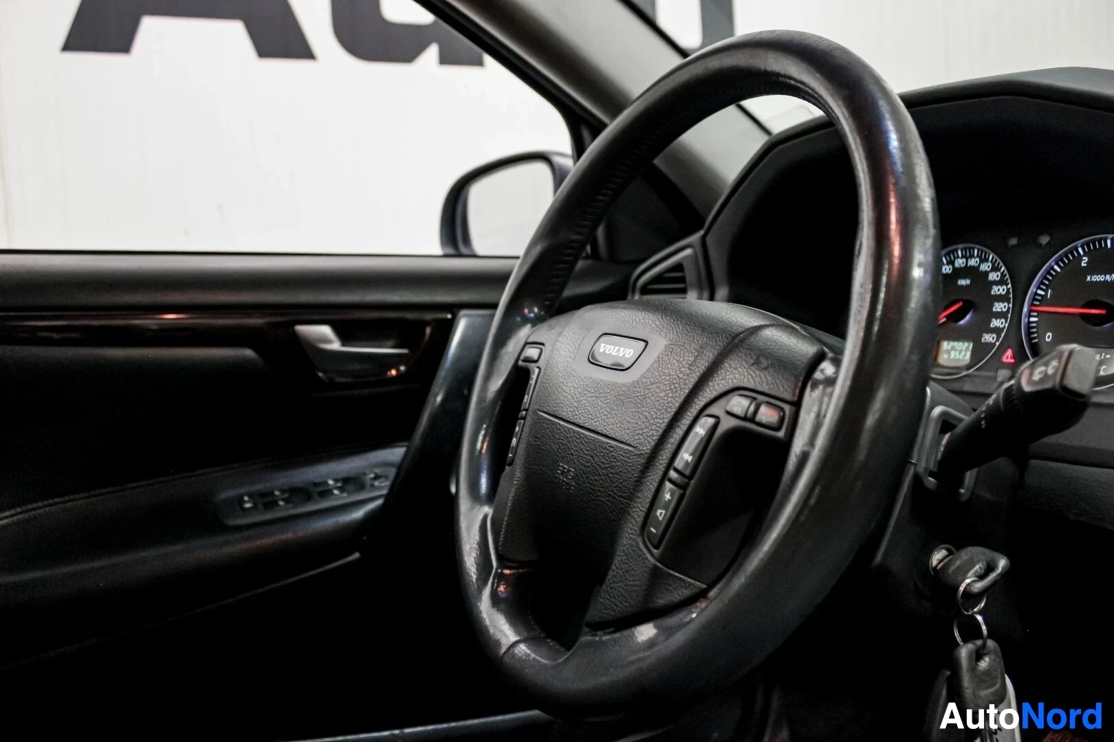 Ohjaamo: Kuva auton ohjaamosta, jossa näkyvät tumma ohjauspyörä Volvo-logolla ja mittaristo.