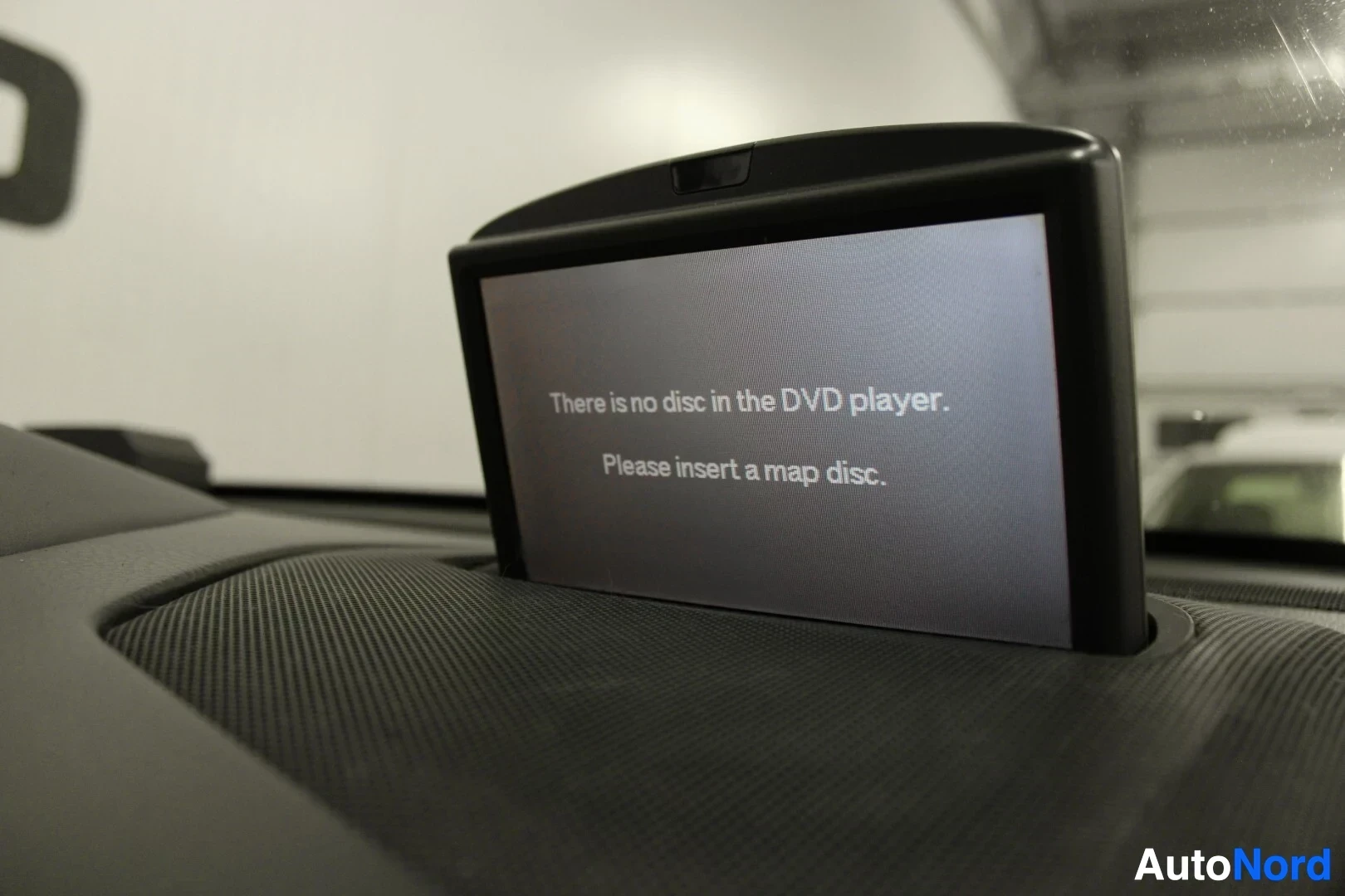 Yksityiskohta: Sisäkuva kojelaudan näytöstä, jossa lukee englanniksi: 'There is no disc in the DVD player. Please insert a map disc.'