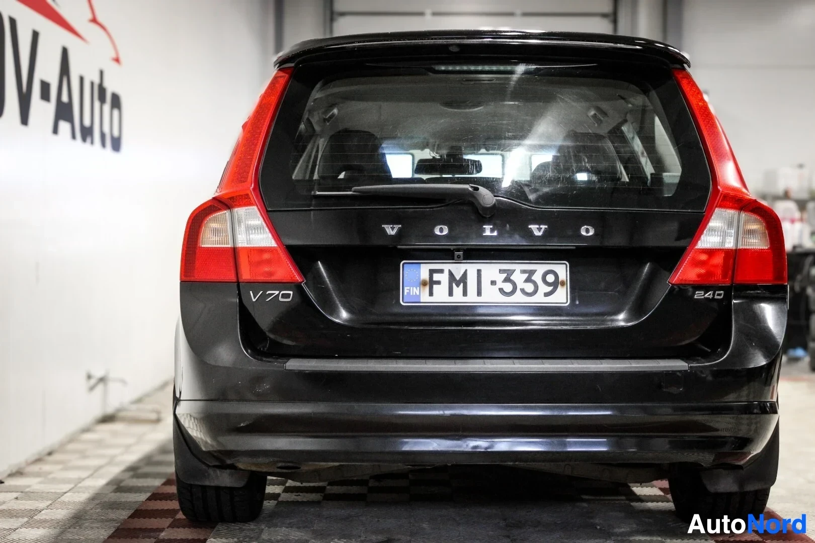 Takaa: Musta Volvo V70 -farmariauto kuvattuna suoraan takaa. Autossa on Volvo-logo ja "V70"- sekä "2.4D"-merkit takaluukussa, ja rekisterikilpi ""