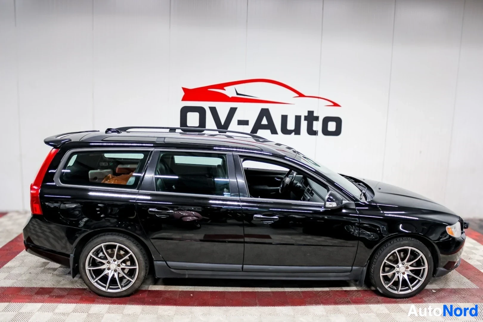 Sivulta: Musta Volvo V70 -farmariauto kuvattuna suoraan vasemmalta sivulta. Autossa on kattokaiteet ja kevytmetallivanteet.