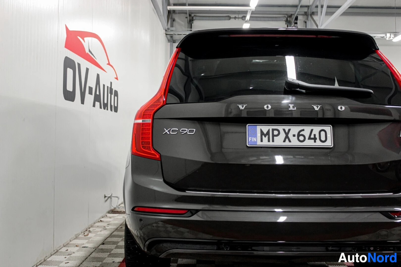 Takaa: Mustan Volvo XC90:n takaosa näkyy sisätilassa. Ajoneuvon rekisterikilpi on ""