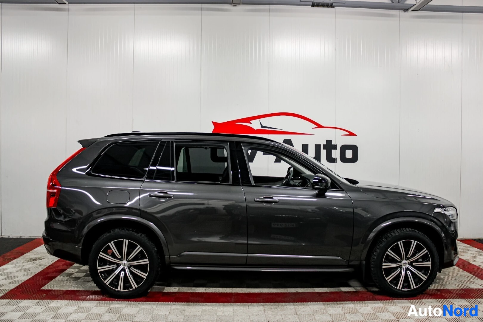 Sivulta: Musta Volvo XC90 näkyy oikealta sivulta sisätilassa. Ajoneuvossa on mustat talvirenkaat ja monipuoliset kevytmetallivanteet.