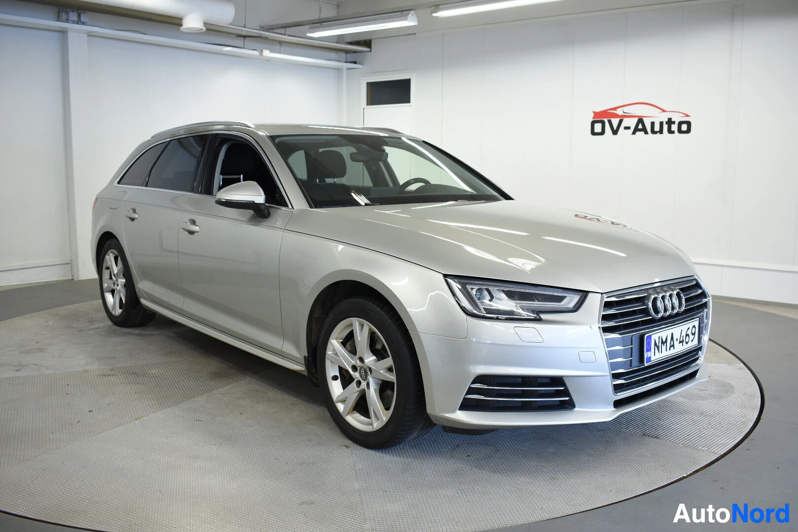 Etuviisto, nokka vasemmalle: Hopeanvärinen Audi A4 Avant -farmariauto kuvattuna etuviistosta oikealta edestäpäin, auton keula osoittaa vasemmalle. Autossa on viisipuolaiset kevytme