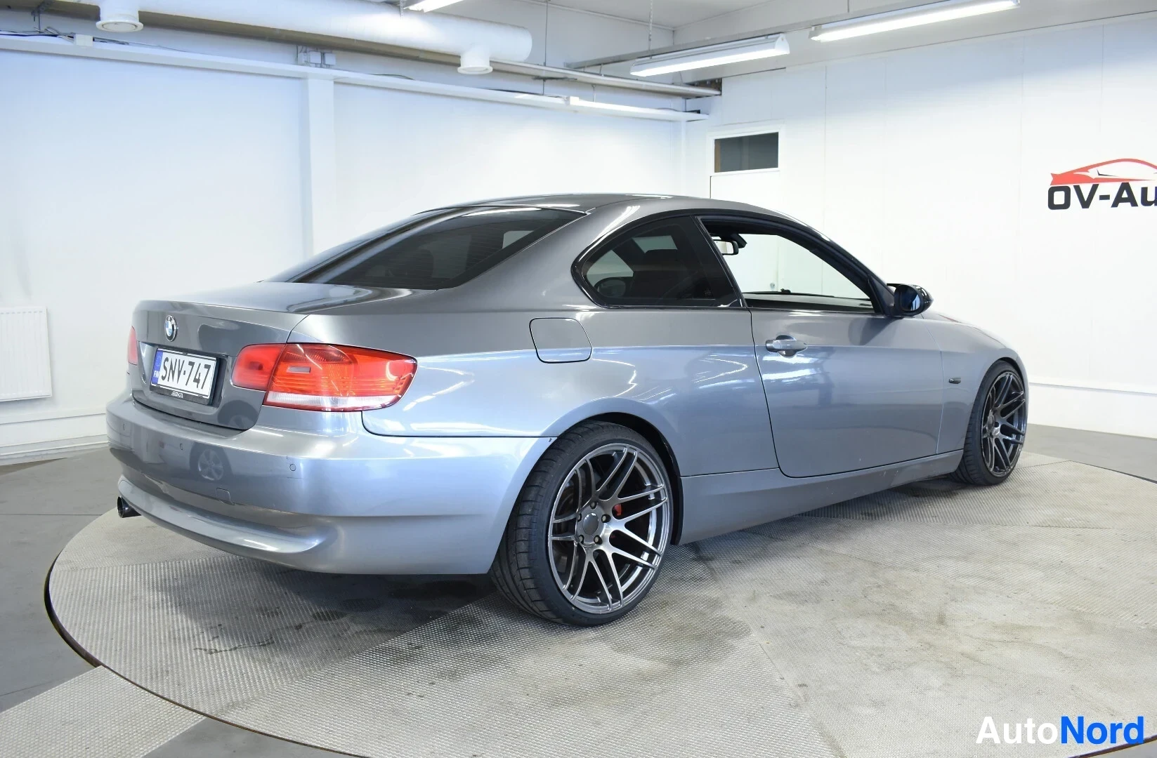 Takaviisto: Harmaa BMW:n coupé takaoikealta kuvattuna, ajovalot ja osa oikeaa kylkeä näkyvissä. Autossa on tummat alumiinivanteet.