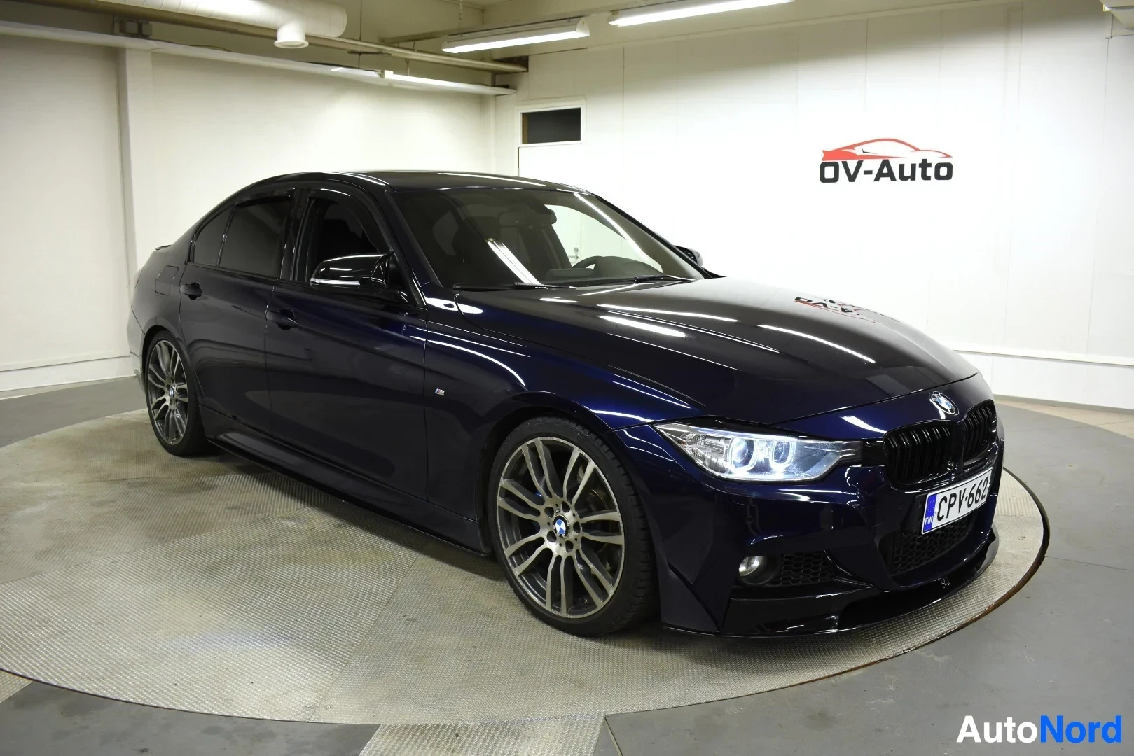 Etuviisto, nokka oikealle: Tummanpunainen BMW 3-sarjan sedan kuvattuna edestä oikealta puolelta sisätiloissa.