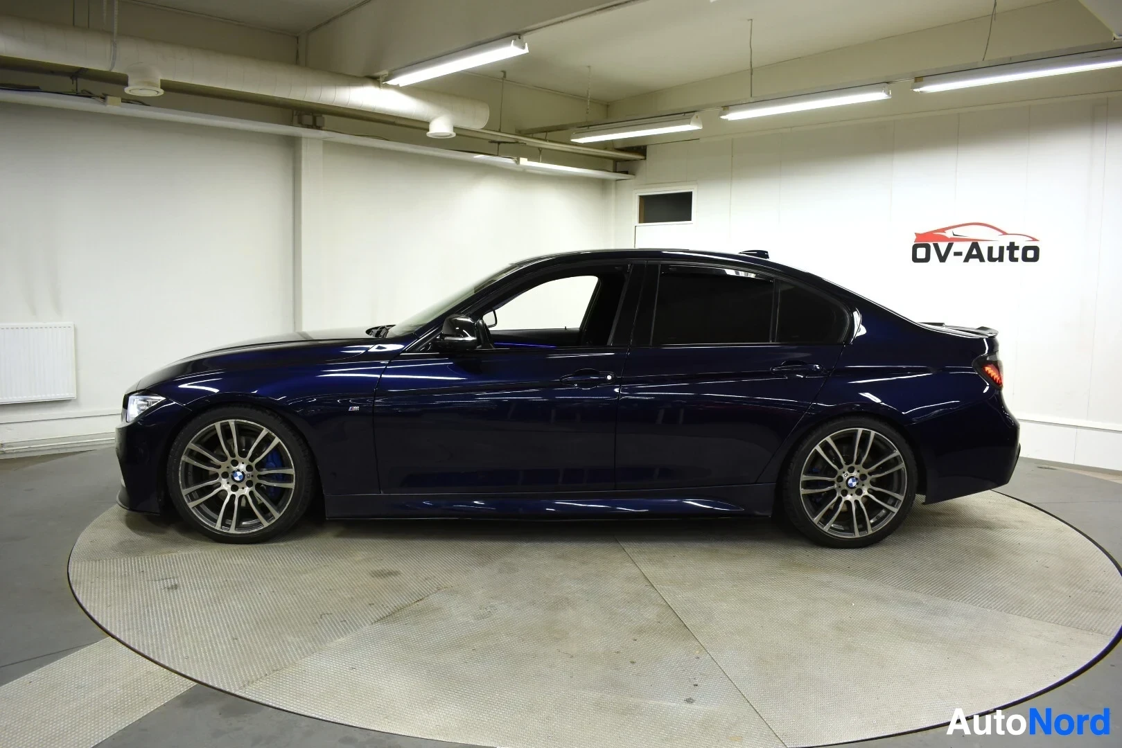 Sivulta: Tummanpunaisen BMW 3-sarjan sedanin vasen kylki sisätiloissa.