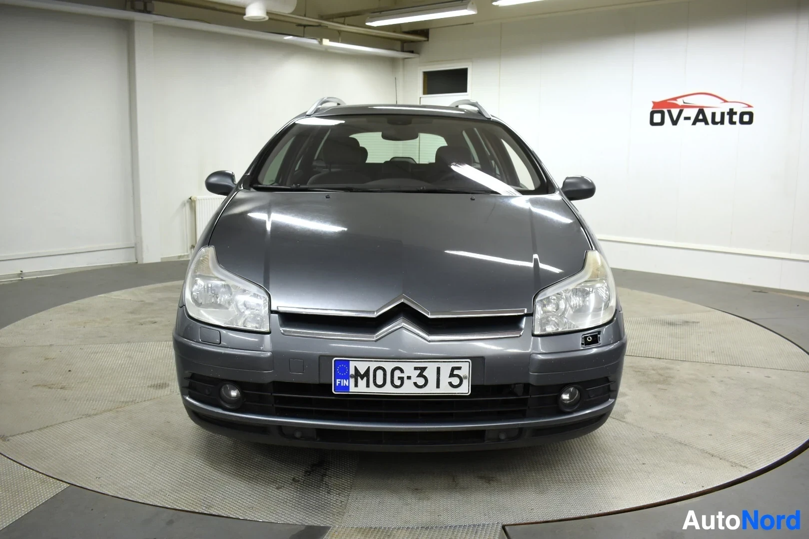 Edestä: Harmaa Citroën C5 farmari on kuvattu edestäpäin, sisätiloissa.