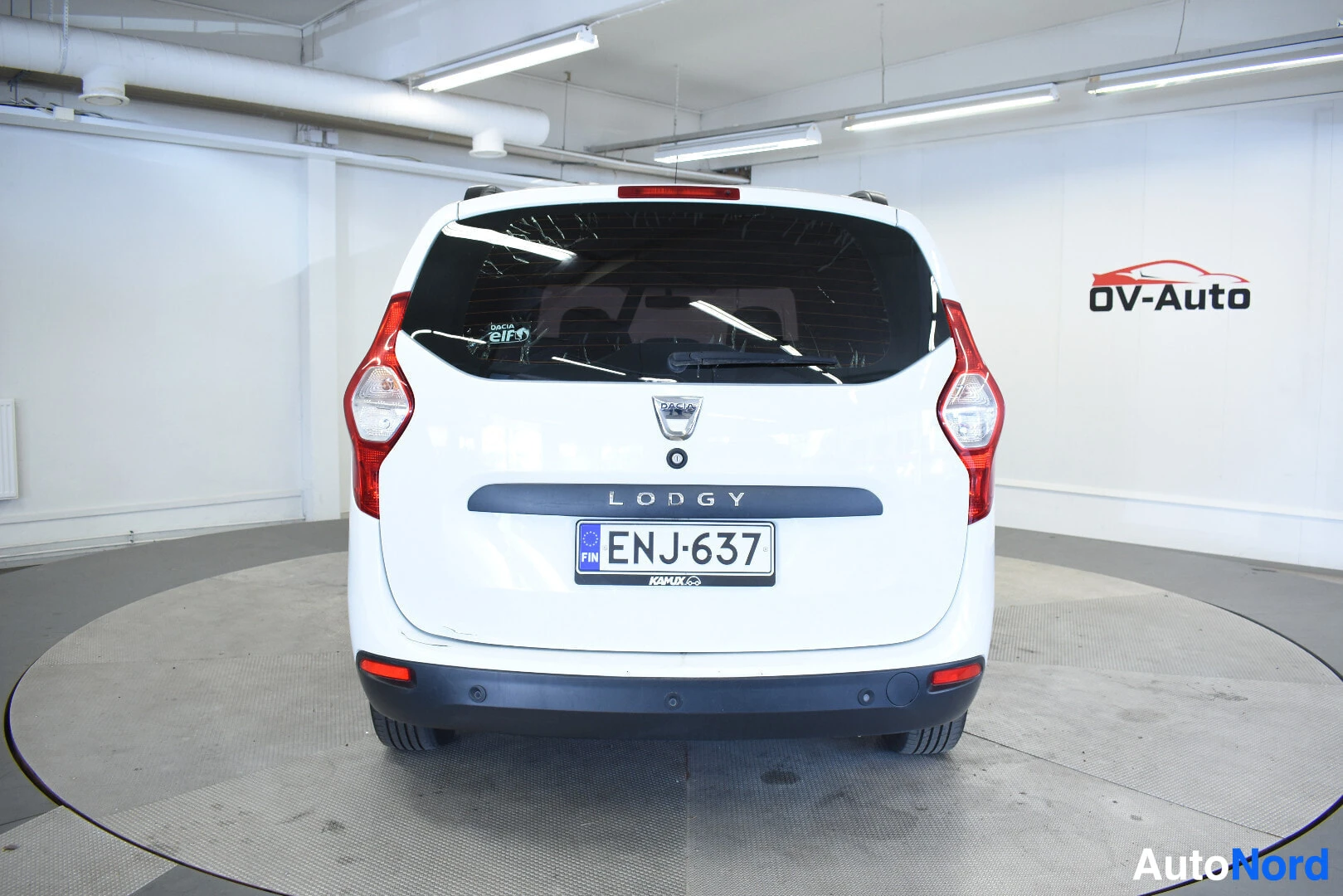 Takaa: Valkoinen Dacia Lodgy henkilöauto kuvattuna suoraan takaa sisätiloissa. Autossa on suomalainen rekisterikilpi "". Takaluukussa lukee "LODGY"