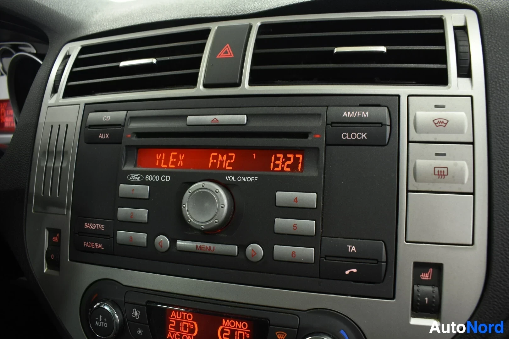 Yksityiskohta: Auton keskikonsolin radio/CD-soitin ja hallintalaitteet, näyttö näyttää "FM2 13:27".